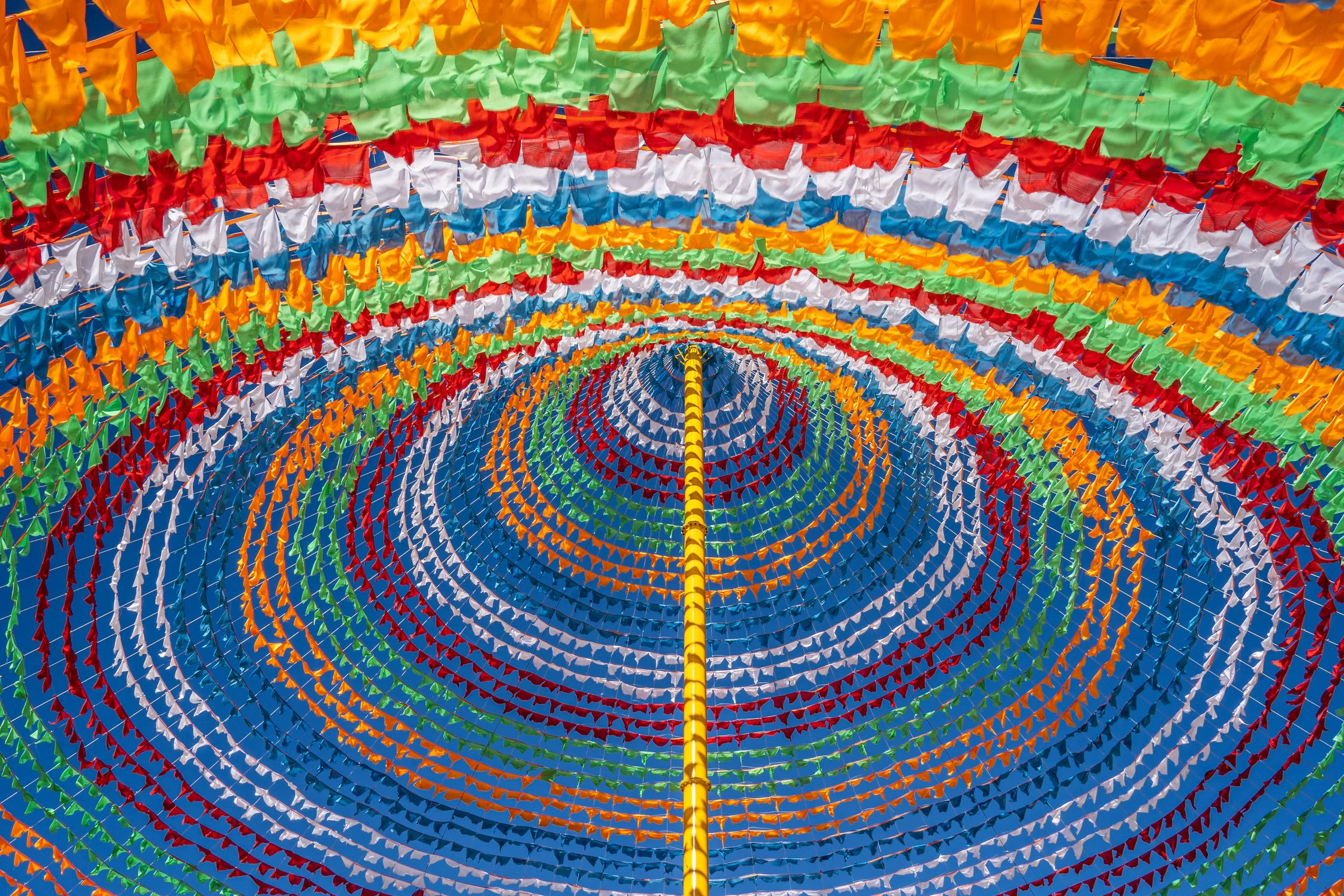 Colorful umbrellas hanging in concentric circles, creating a vibrant canopy with a yellow pole in the center.