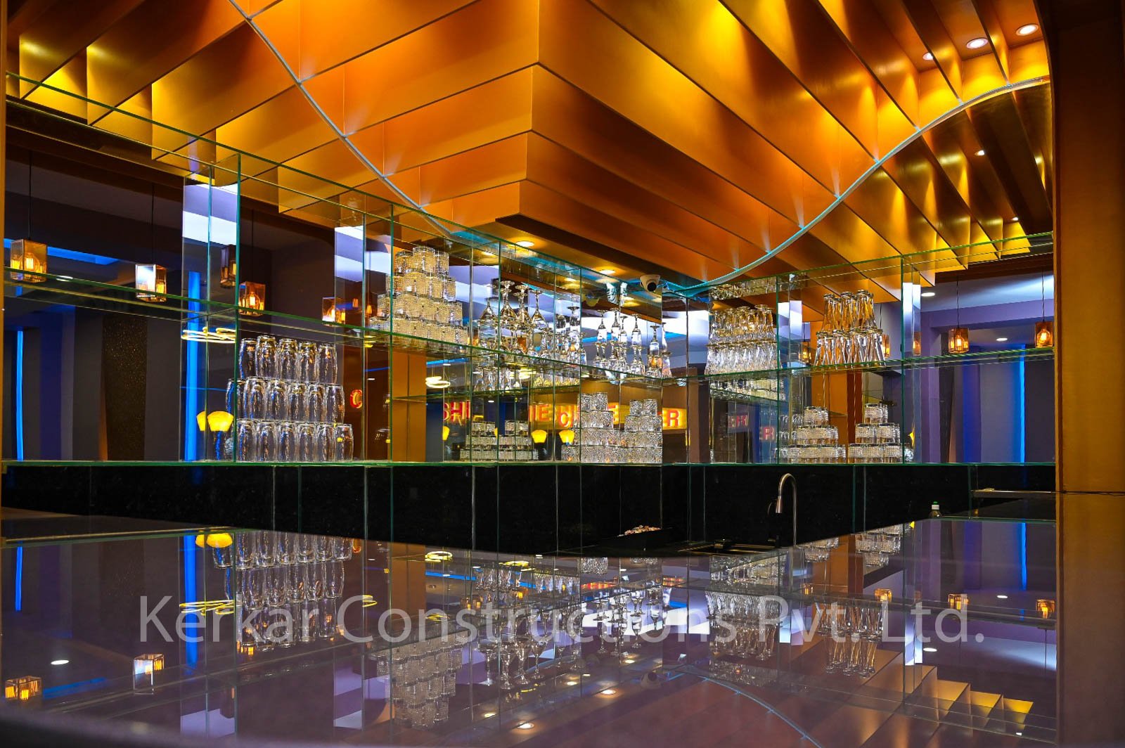 Interior view of a bar with glass shelves holding various glasses, illuminated with warm, colorful lighting, and reflective surfaces.