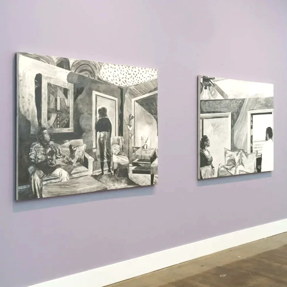 Two black and white paintings by artist glyneisha, depicting interior scenes with people, hung on a plain lavender wall in an art gallery.