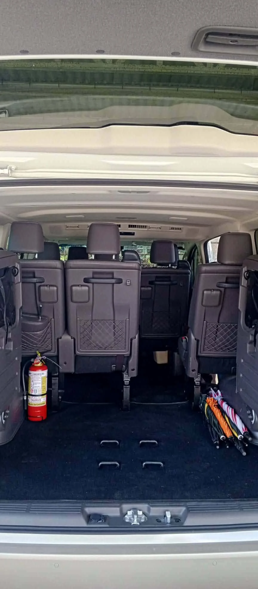 The back of a minivan with the rear seats upright, showing a fire extinguisher on the left side and a folded umbrella or sunshade on the right side.