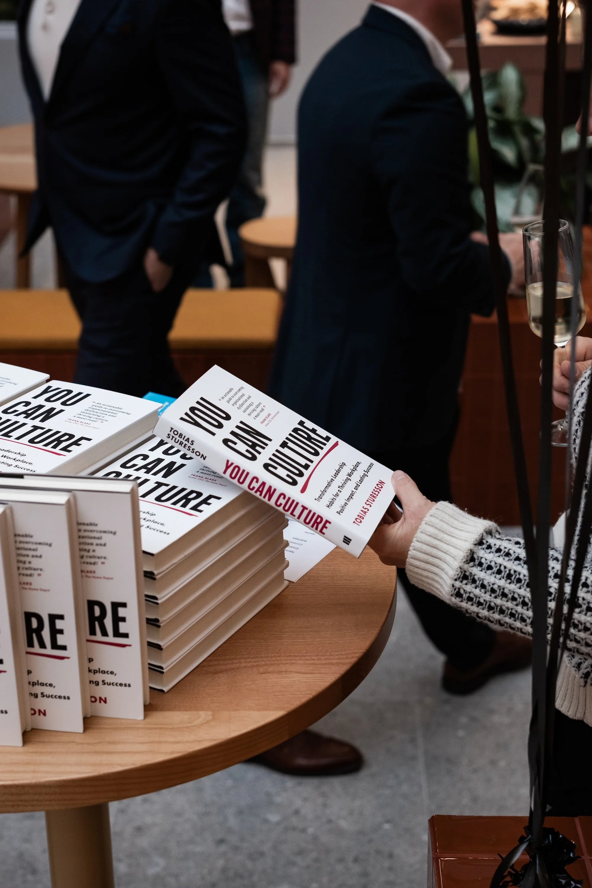 A person holding the'You Can Culture' book at a table with several copies of the same book stacked.