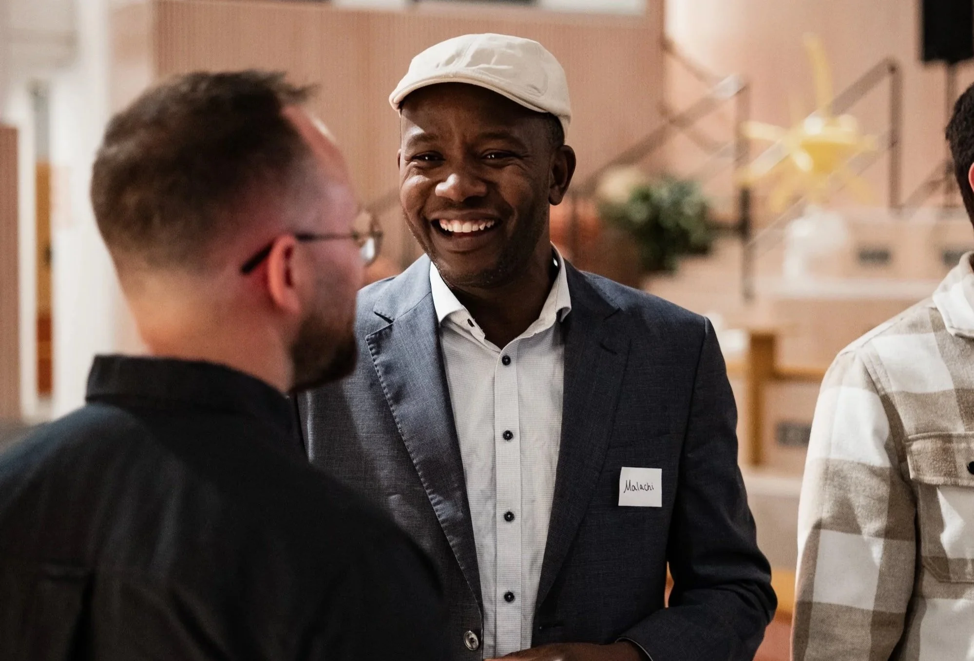 Two men engaged in conversation at You Can Culture launch event, with one smiling broadly and wearing a white hat and a name tag.