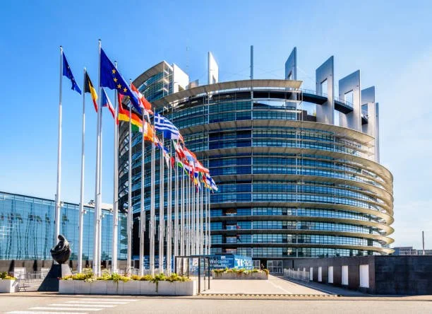 Modern building with multiple European flags on flagpoles in front.