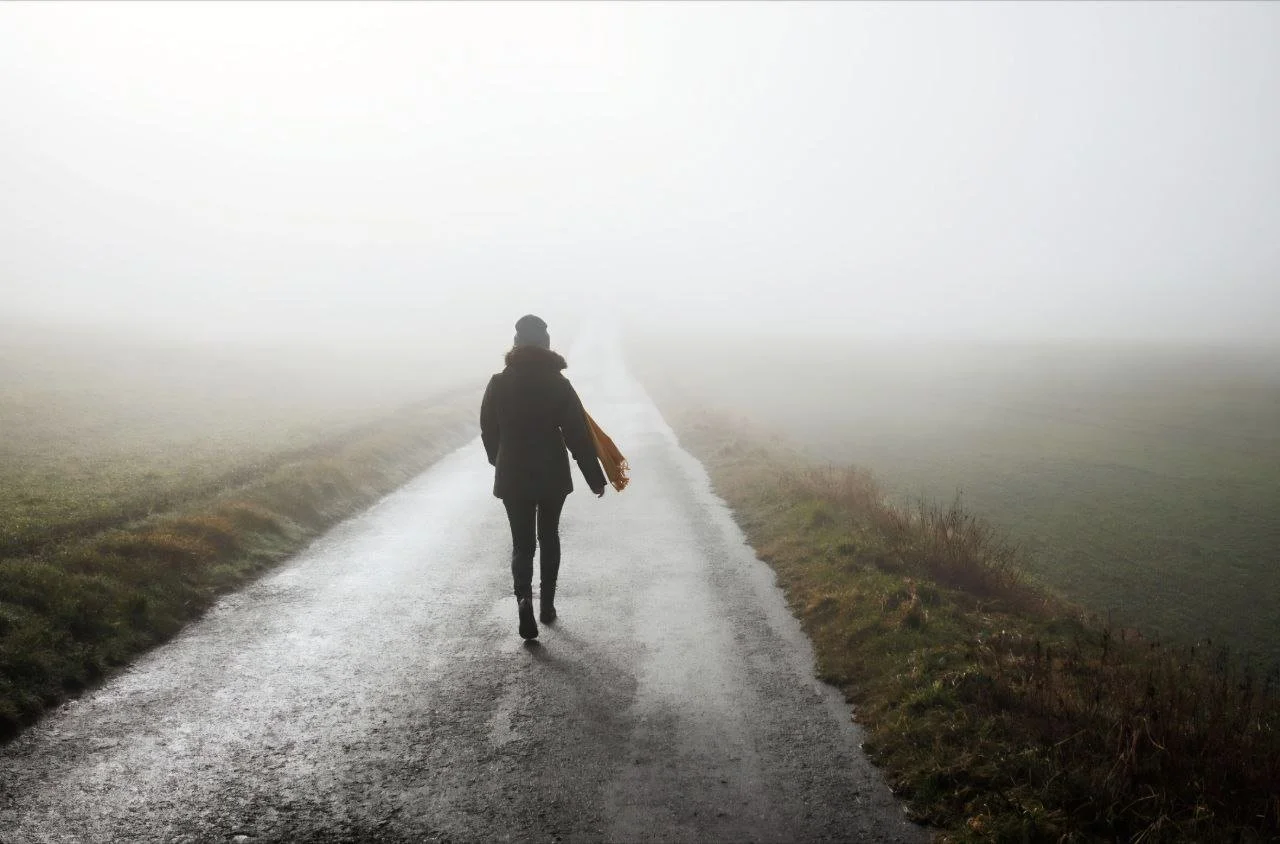 Eine Person läuft in einem nebligen Landschaft auf einer asphaltierten Straße.