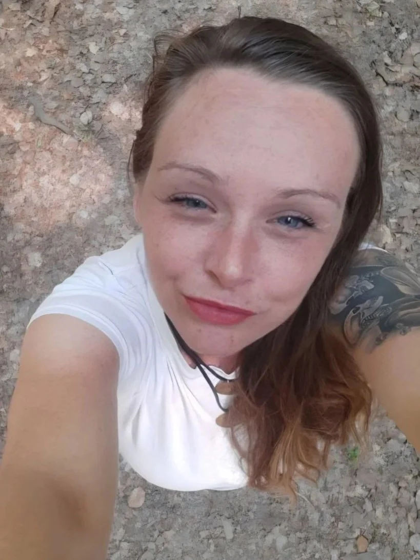 Junge Frau mit braunen Haaren, blauen Augen und Sommersprossen nimmt einen Selfie-Foto draußen auf kargem, felsigem Boden auf.