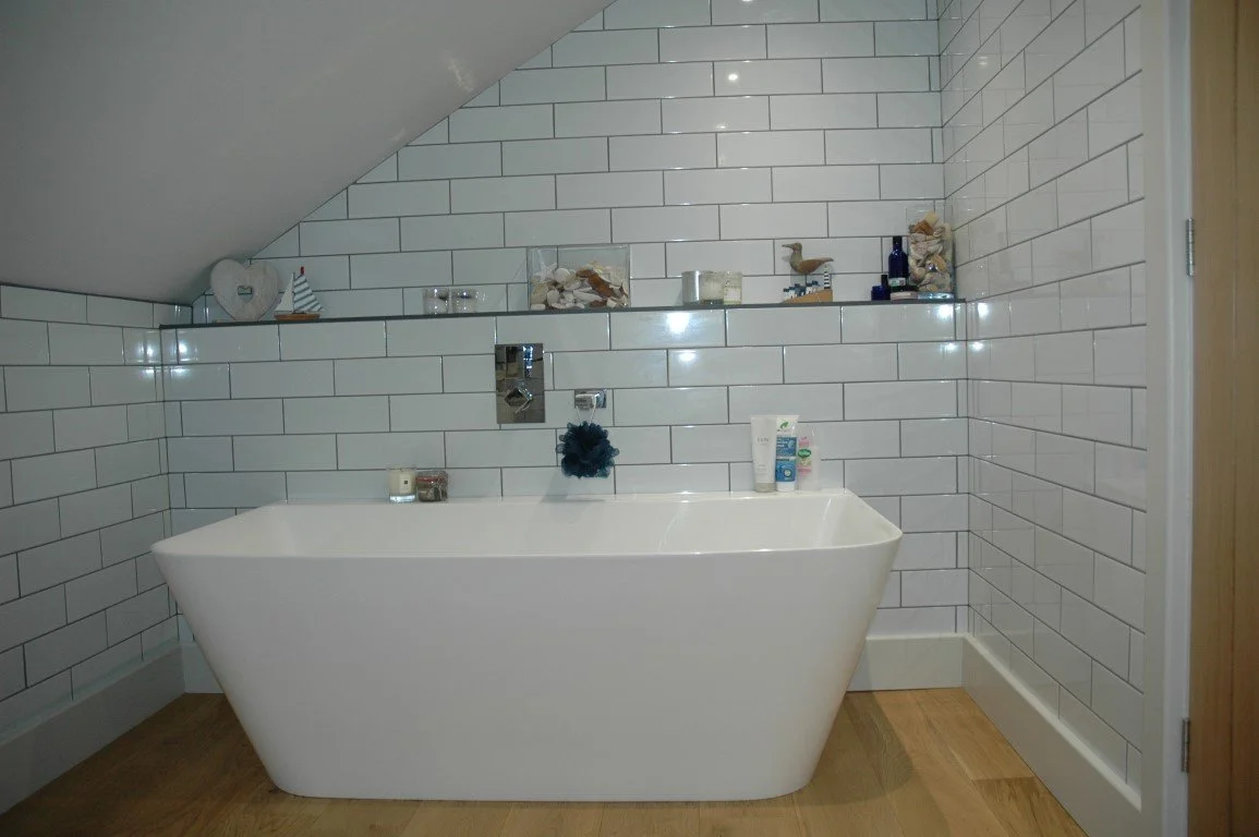 Modern bathroom with a white bathtub, tiled walls, and decorative items on a shelf above the tub.