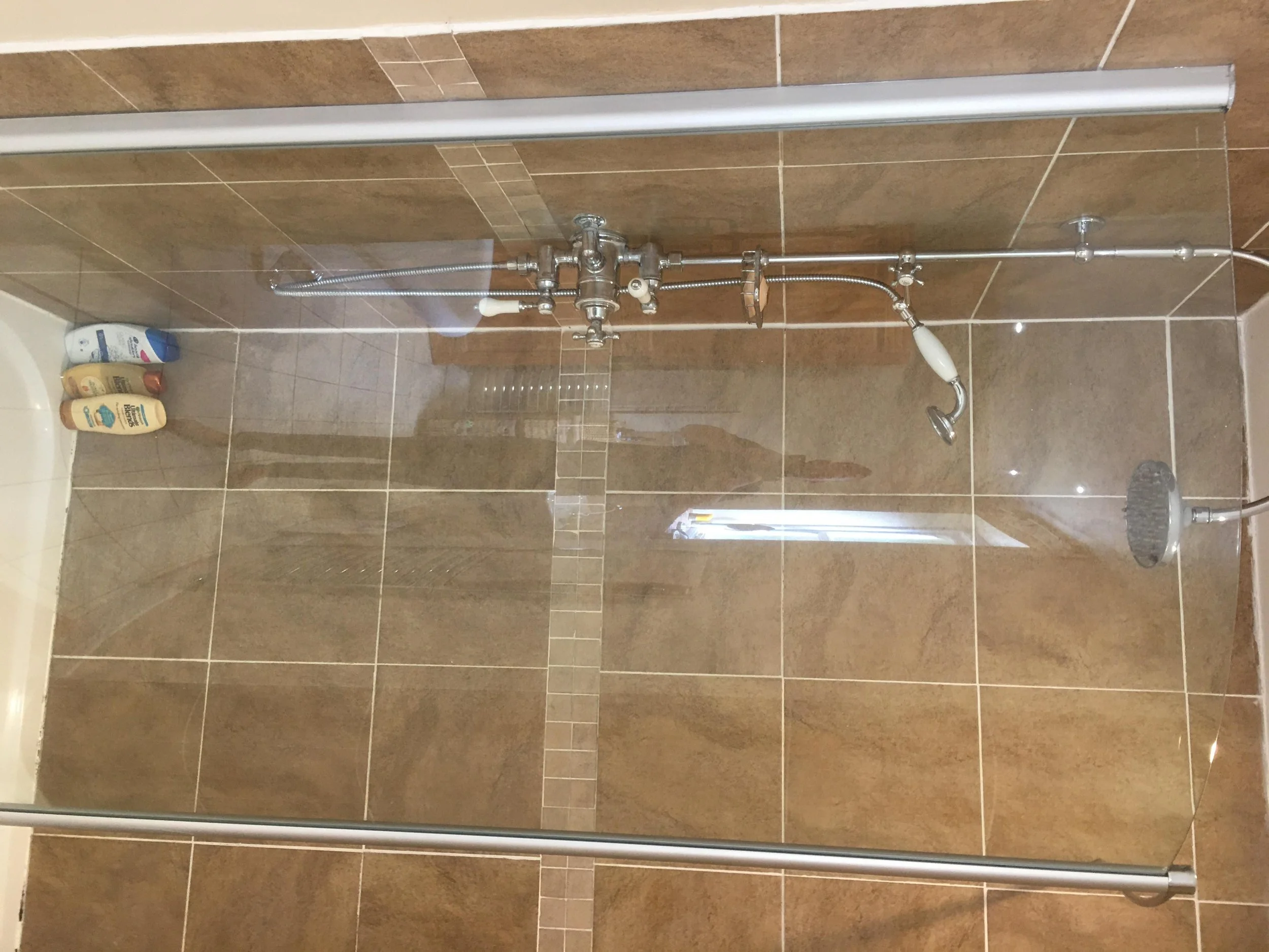 Bathroom shower with brown tiled walls, glass enclosure, and a shower head.