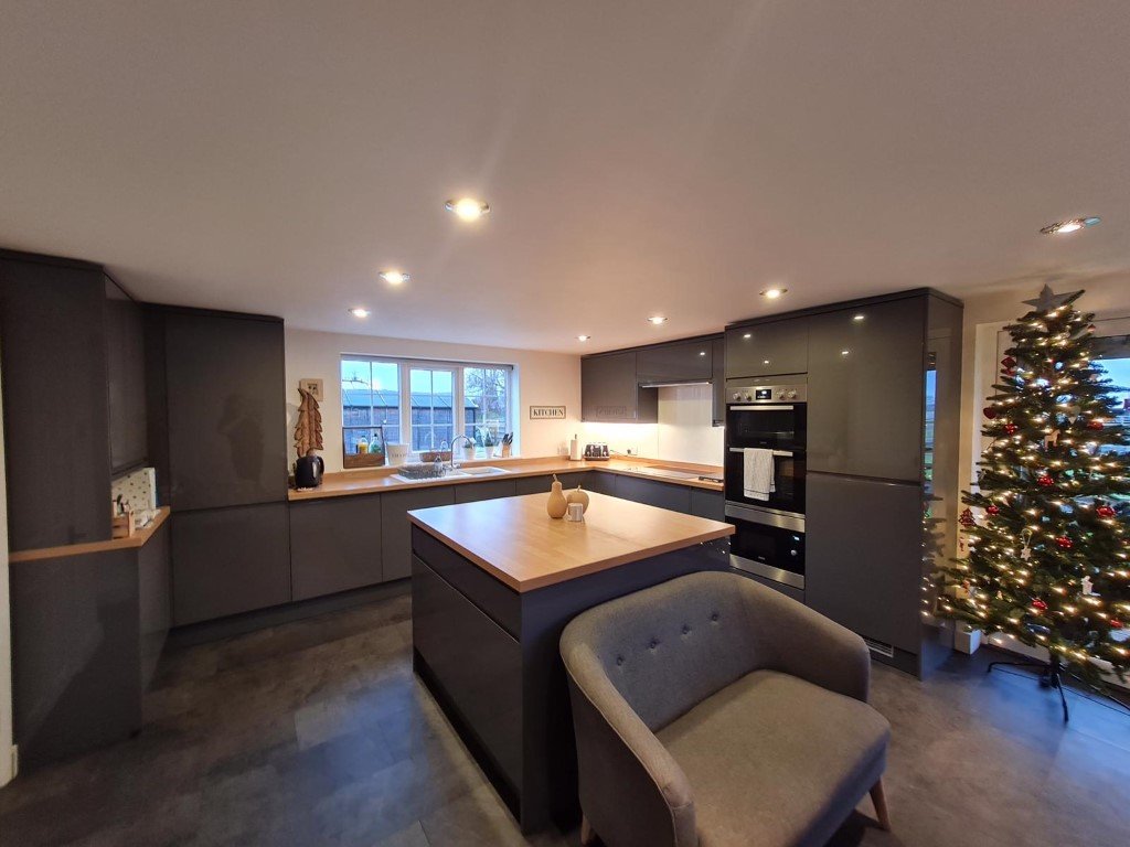 Modern kitchen with gray cabinets, a large central island with wooden top, Christmas tree with ornaments, and a window overlooking a backyard.