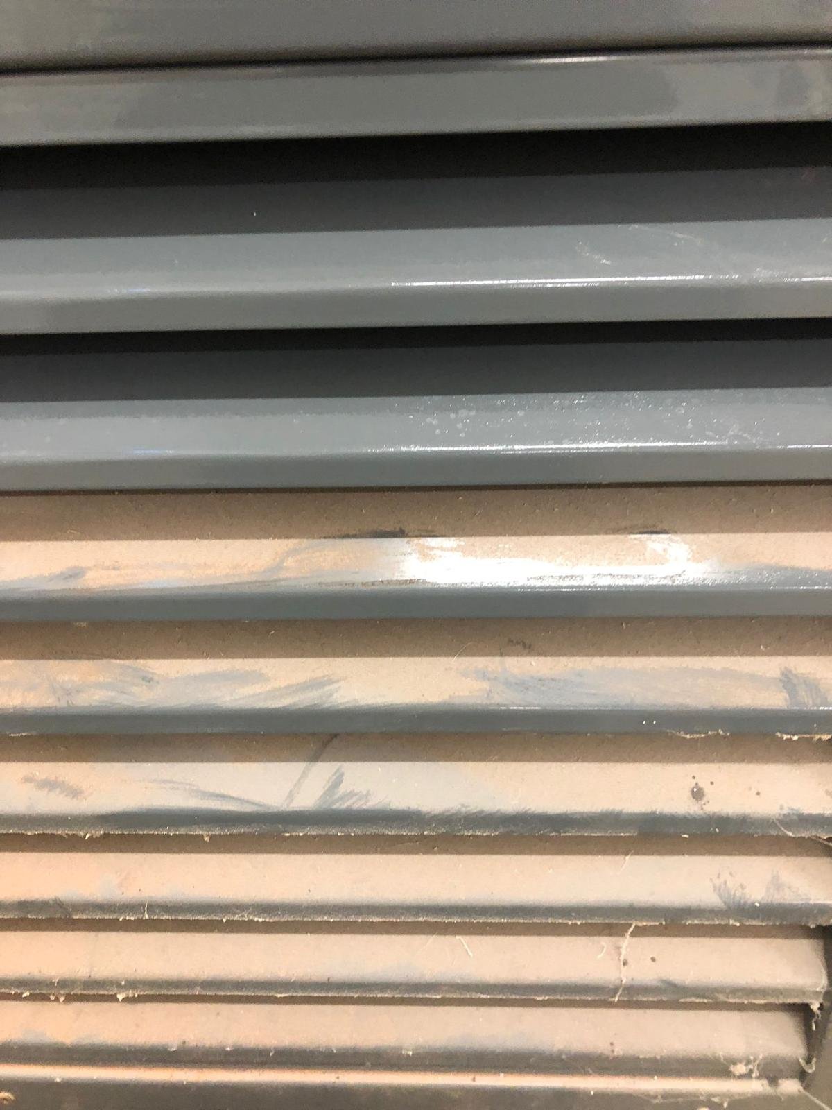 Close-up of horizontal metal vents or louvered panels in gray and beige, with dust and minor scratches.