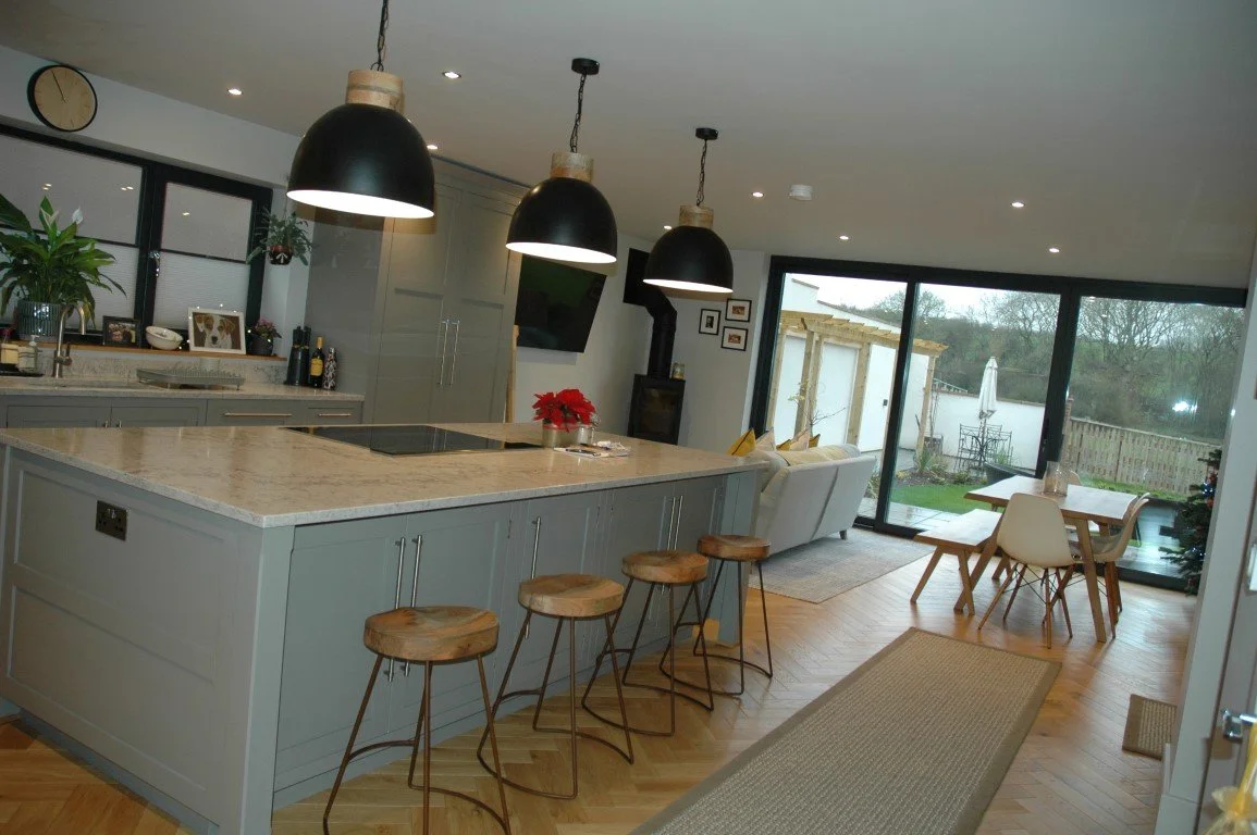 Open-concept kitchen and dining area with gray cabinetry, a marble countertop island, black pendant lights, and a view of the backyard with patio furniture and a garden.