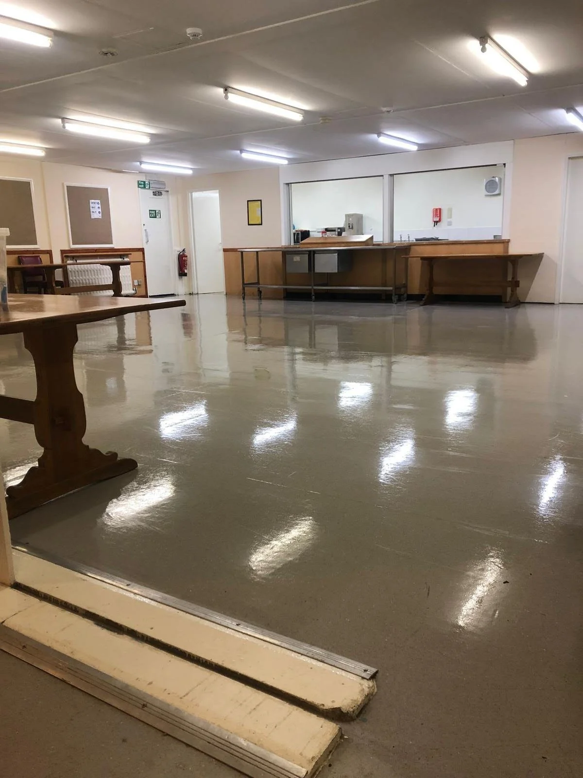 Empty room with a shiny polished floor, wooden furniture, and a service window in the wall.