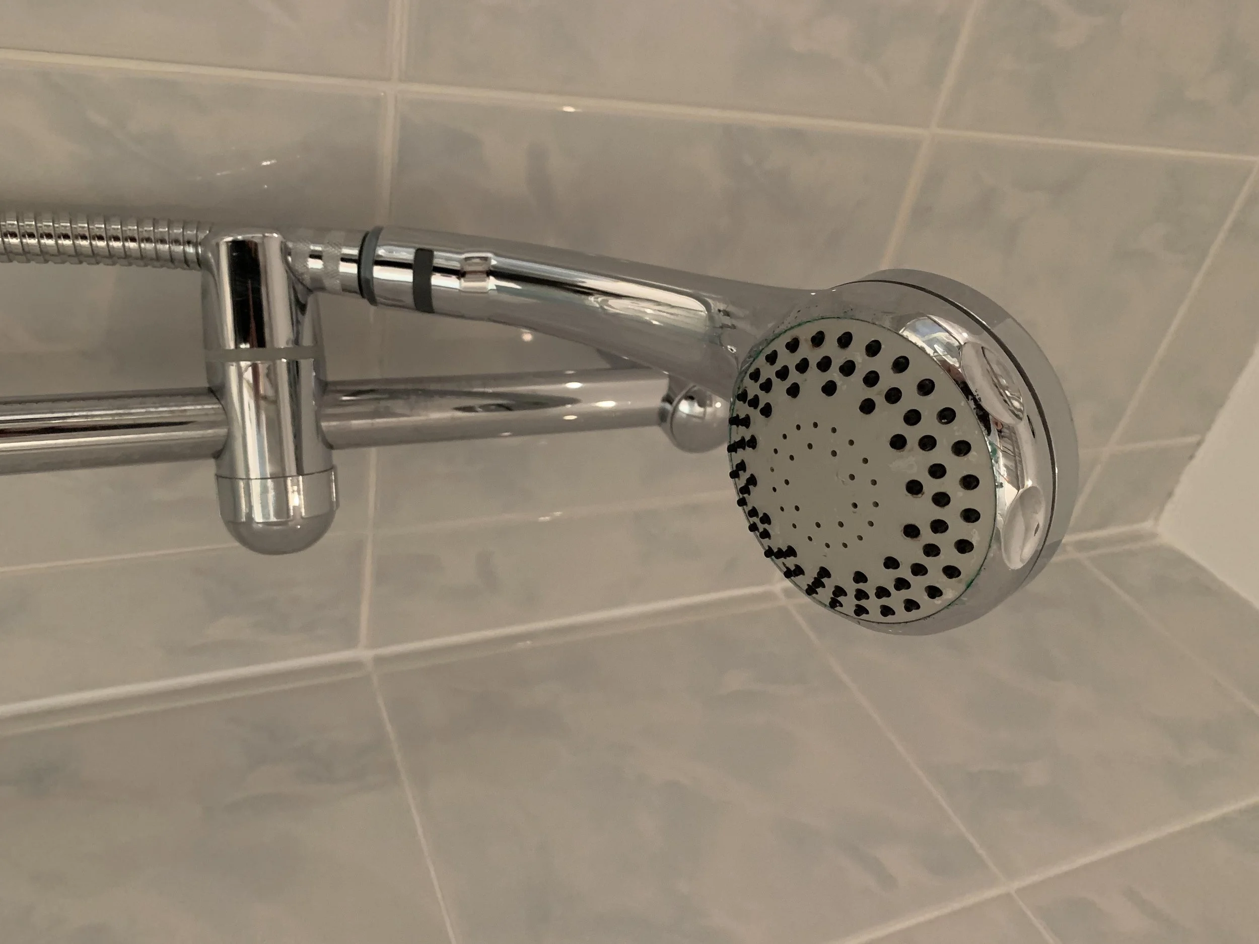 Showerhead mounted on a bathroom wall with beige tiled background.