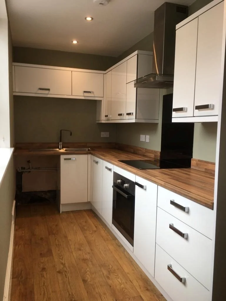 Kitchen with white cabinets, wooden countertops, stove, oven, extractor fan, and wooden flooring.