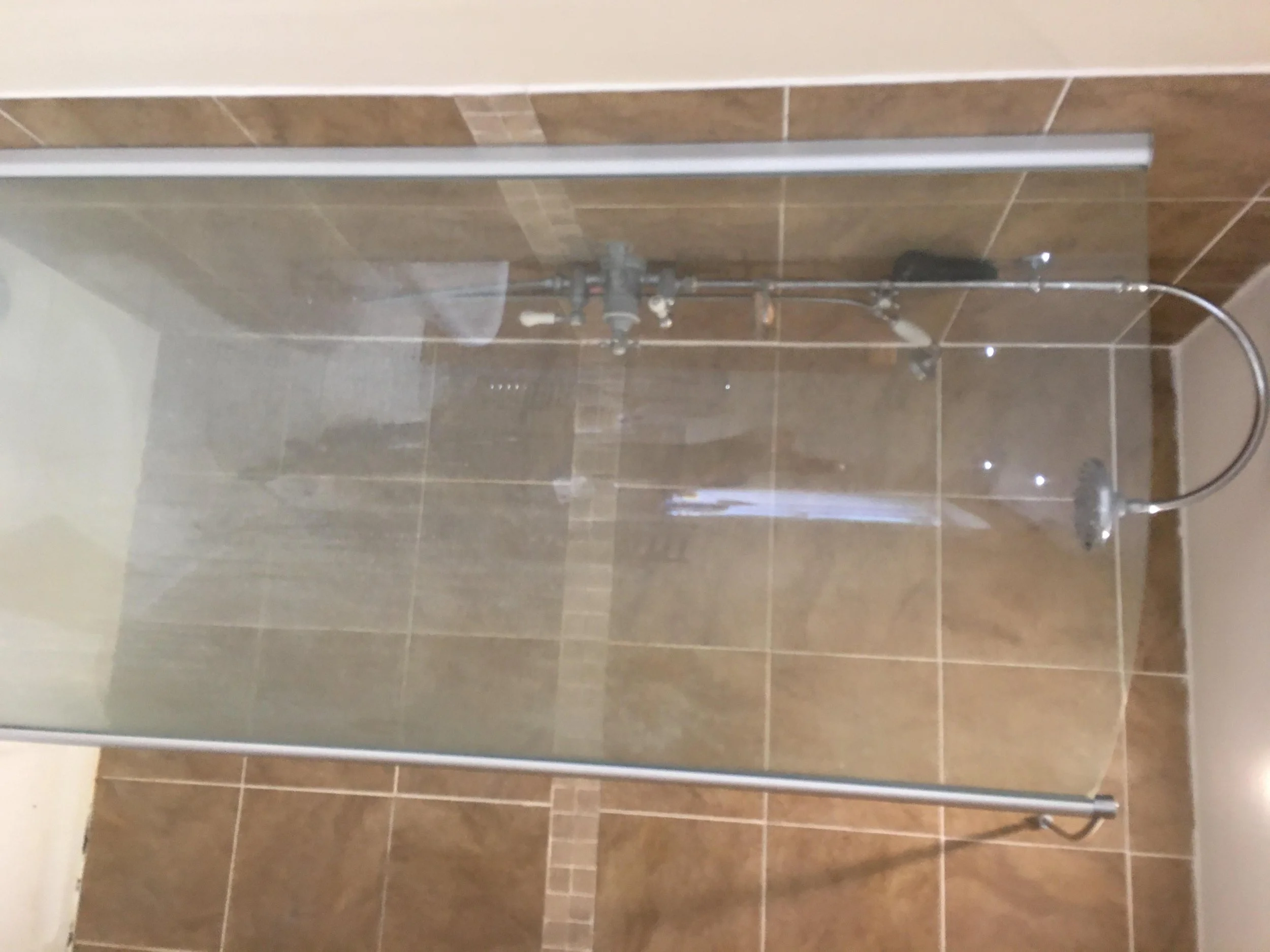 Glass shower enclosure with brown tiled walls and floor, and a chrome rainfall showerhead.