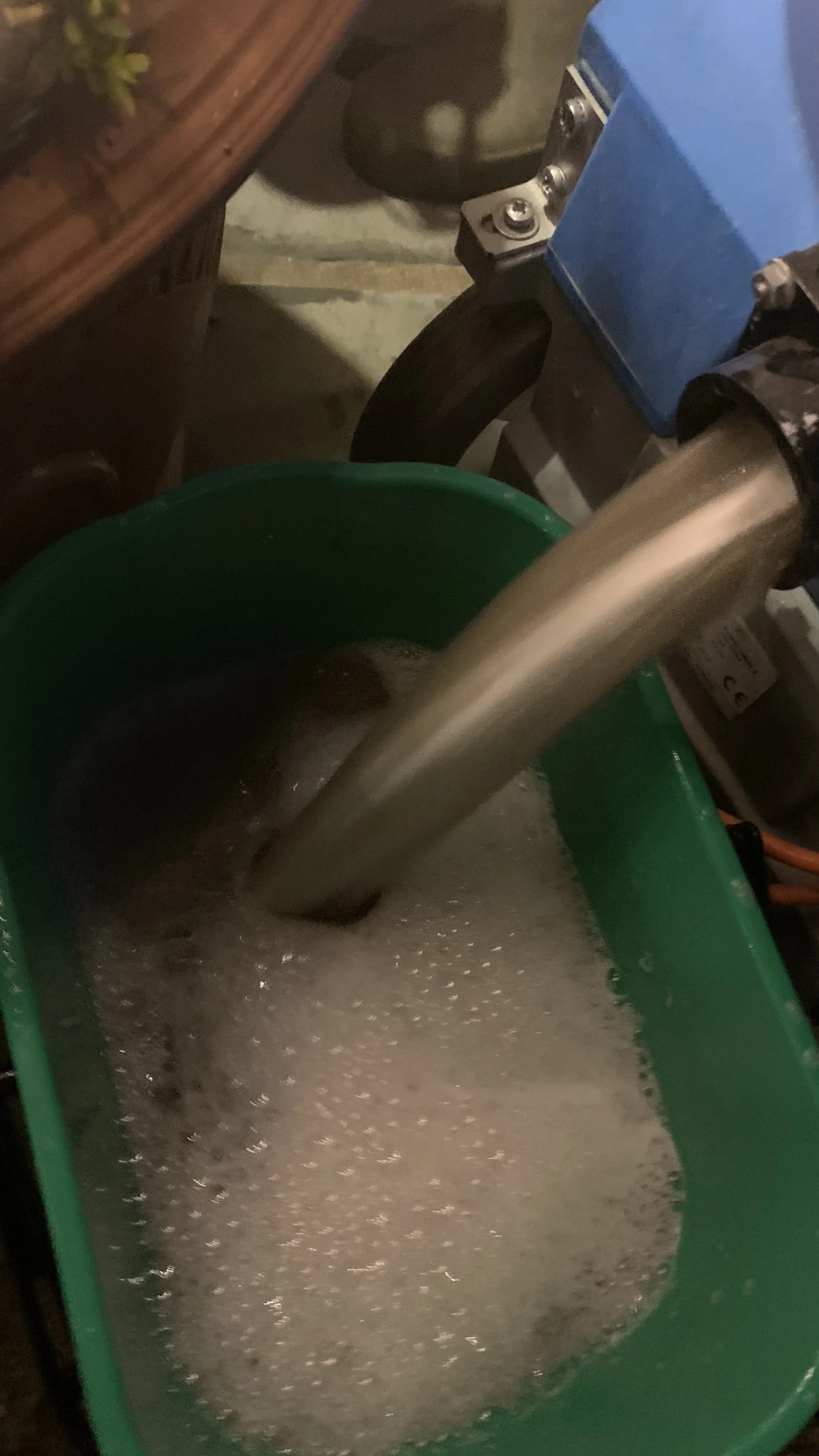 A metal pipe is pouring water into a green bucket, creating foam on the surface.
