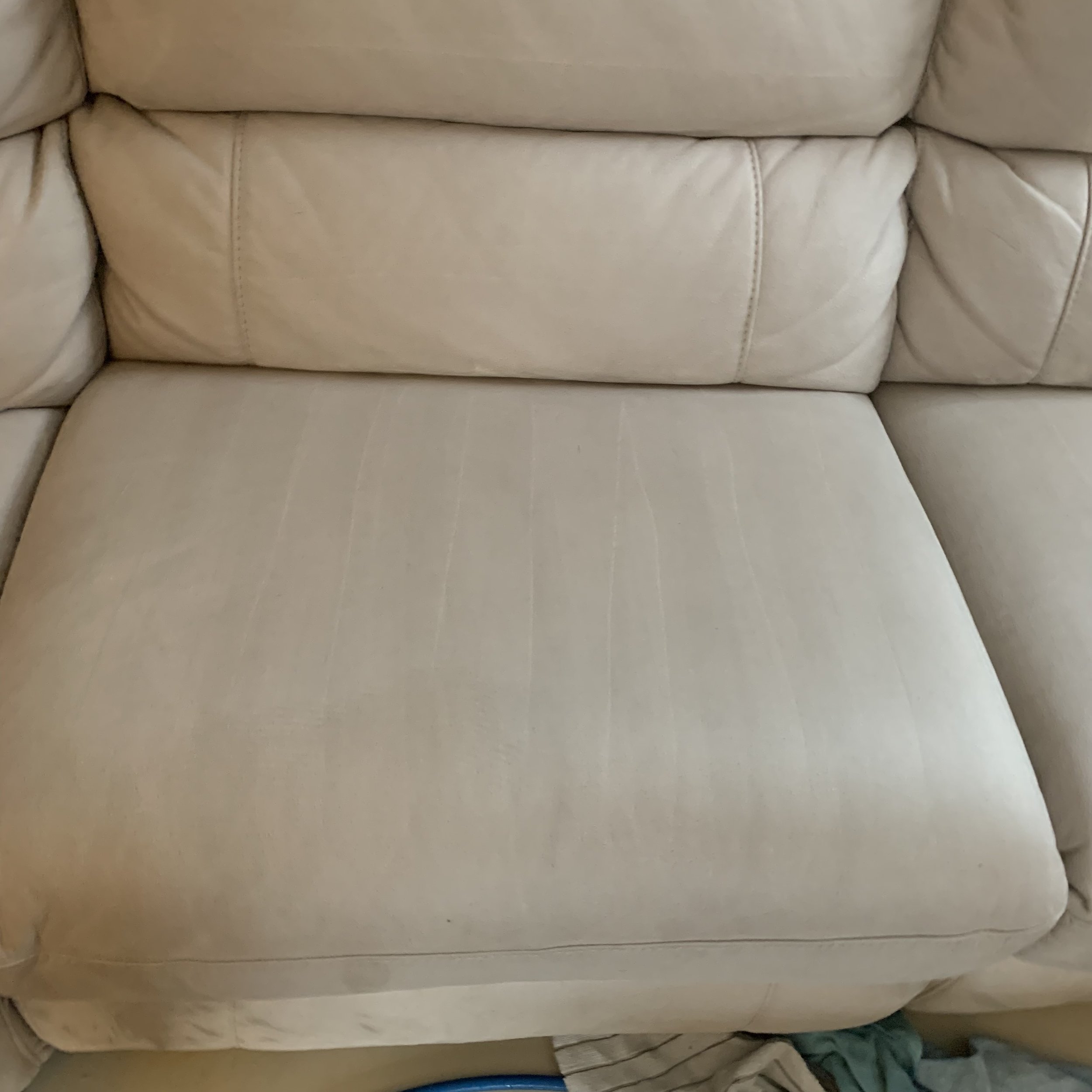 Close-up of a beige leather sofa, showing the seat cushion and some backrest cushions with visible stitching.