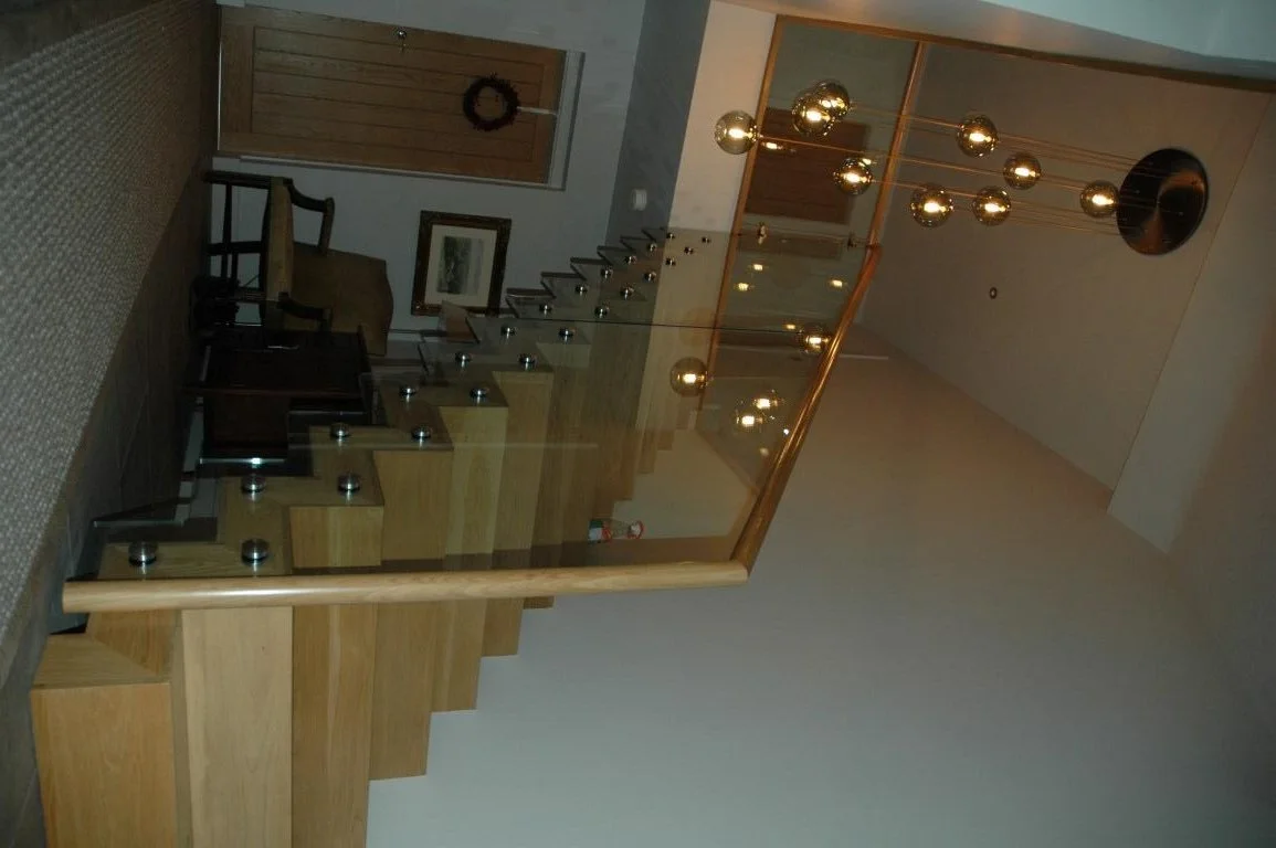 Interior view of a staircase with wooden steps, a glass railing, and a modern gold chandelier with multiple bulbs hanging from the ceiling.