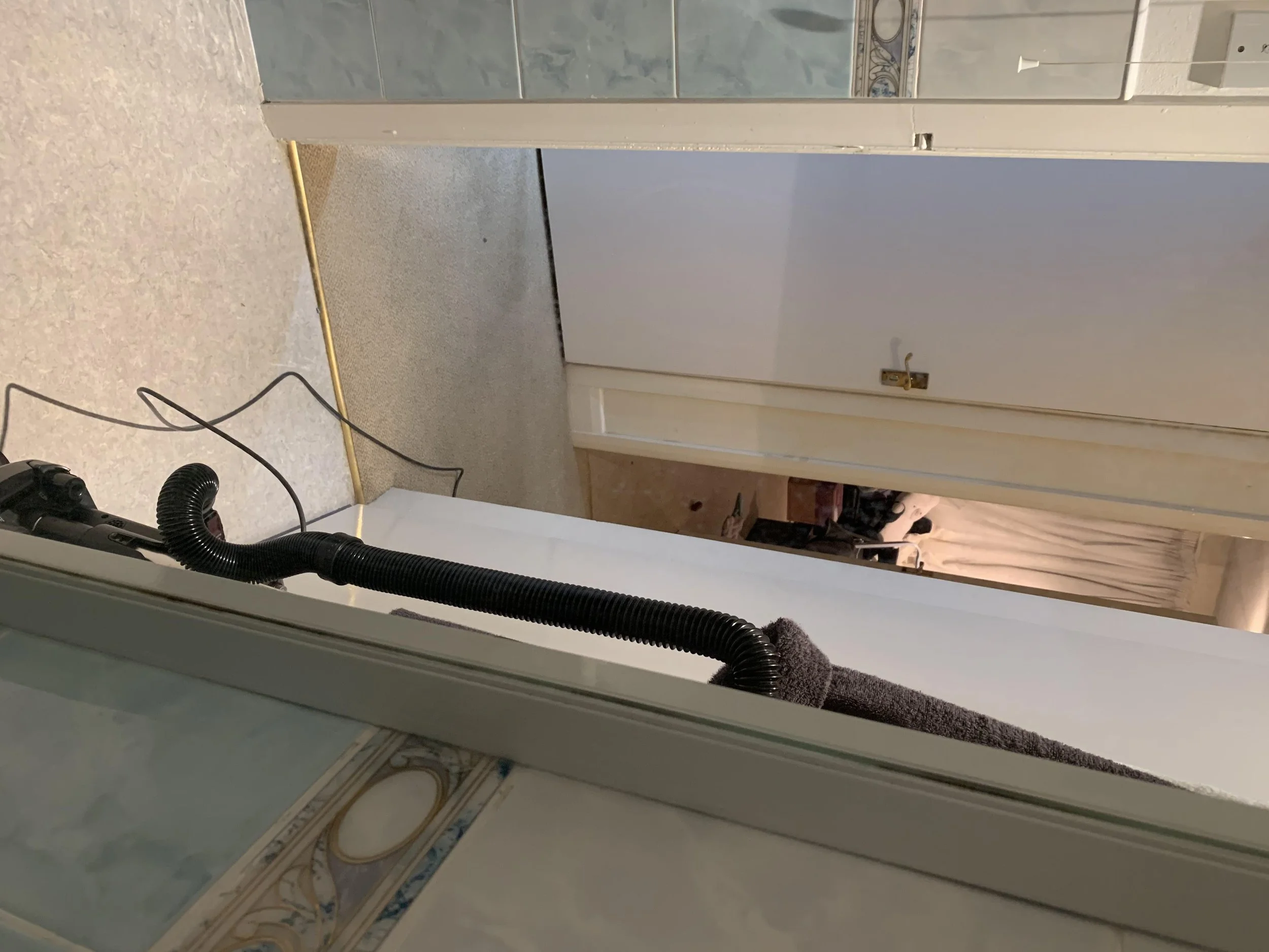 A black vacuum cleaner hose resting on a beige countertop in a kitchen, with the hose extending across the counter and a gray yarn or cloth attached to it.