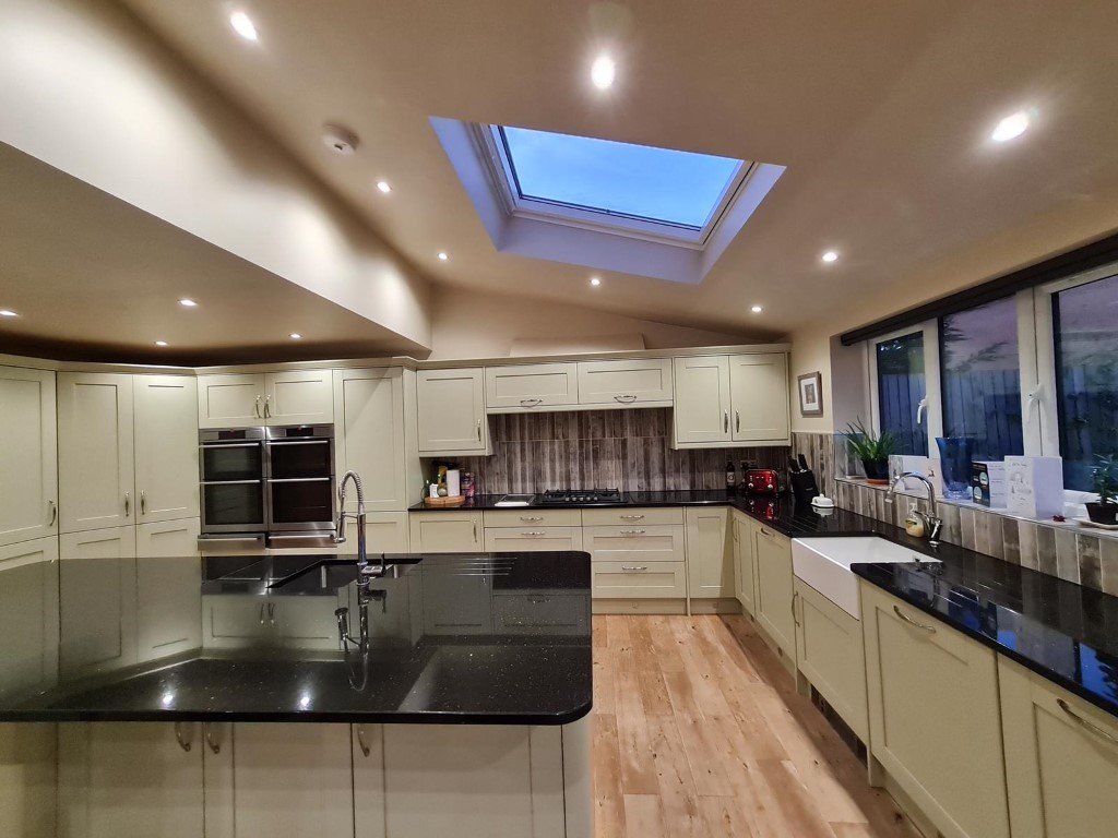 Modern kitchen with cream cabinets, black countertops, hardwood floors, and a skylight in the ceiling.