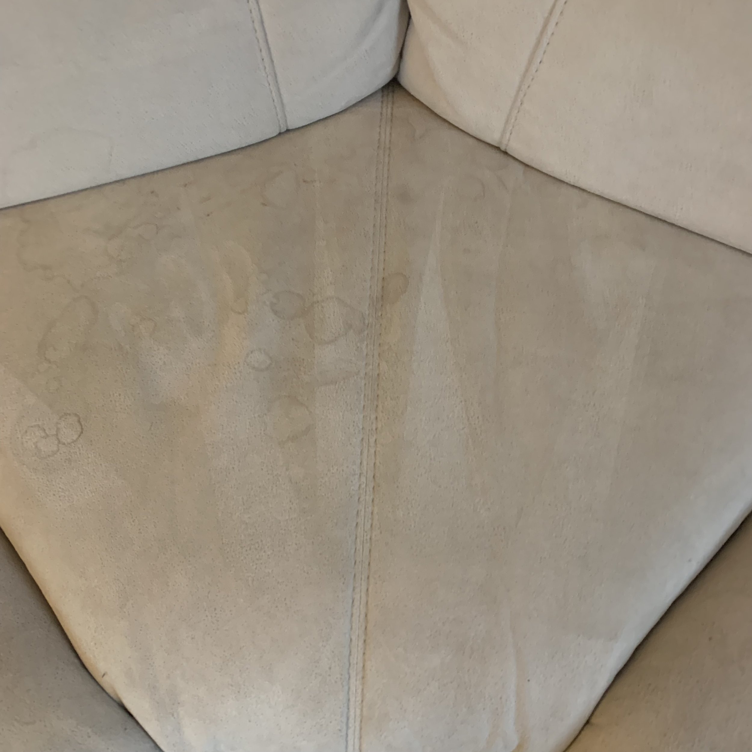 Close-up of a beige fabric sofa with water stains and marks on the armrest.