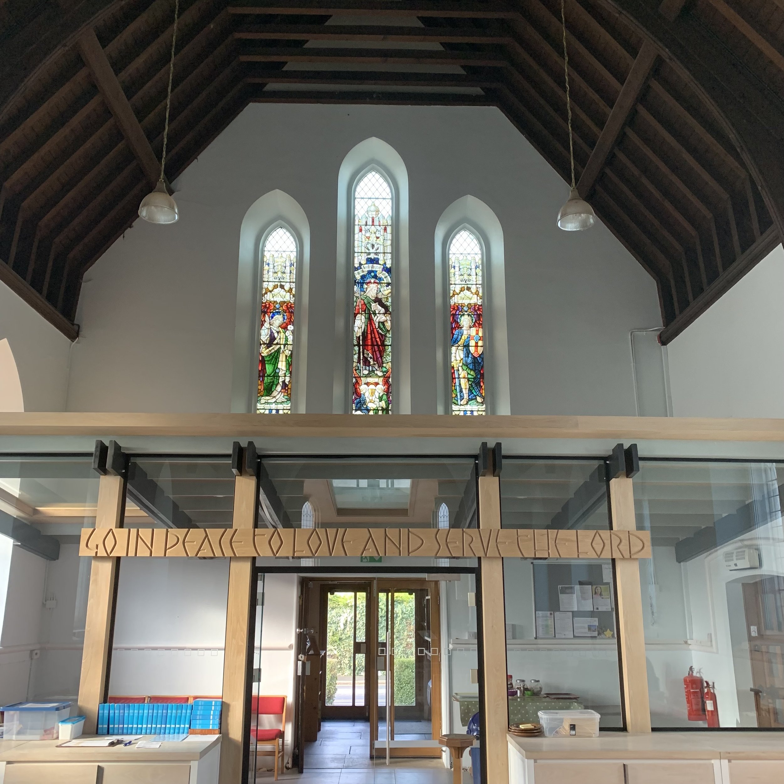 Interior of a church with stained glass windows and a wooden loft with a handwritten sign that says 'Go in peace, go love and serve the Lord'.