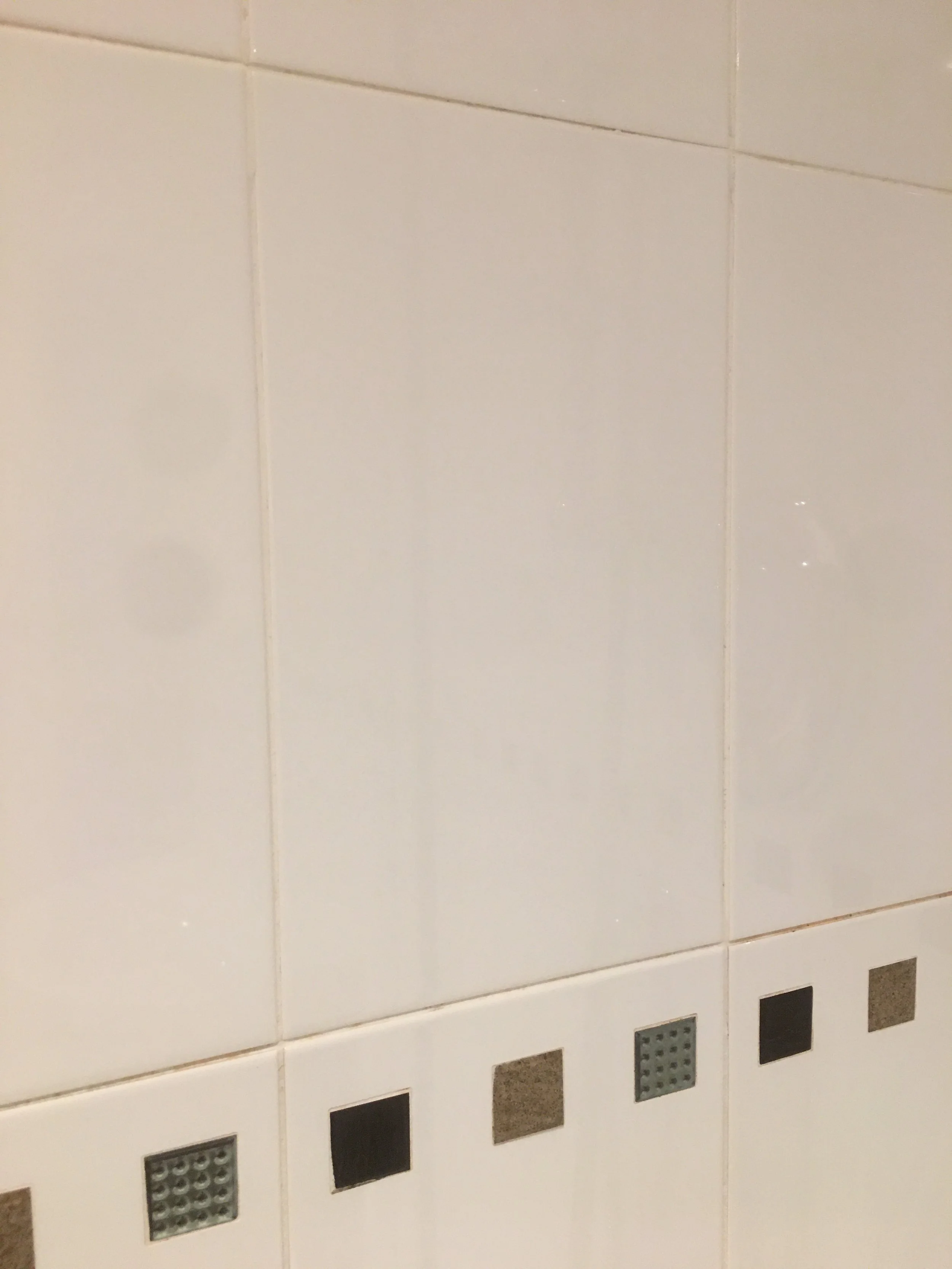 Close-up of a tiled wall with small decorative tiles at the bottom, some of which are black, gray, or brown, with a few featuring a textured pattern.