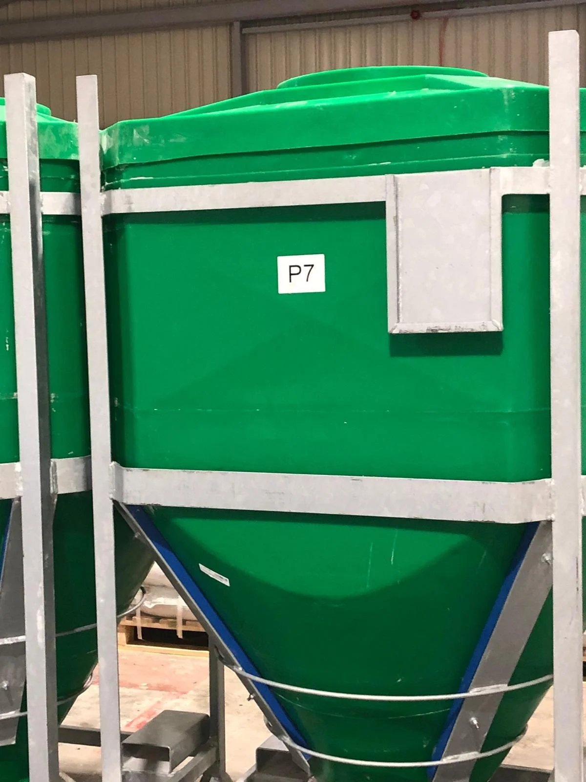 A large green industrial hopper with a metal frame and a label reading 'P7' on the front, situated inside a warehouse.