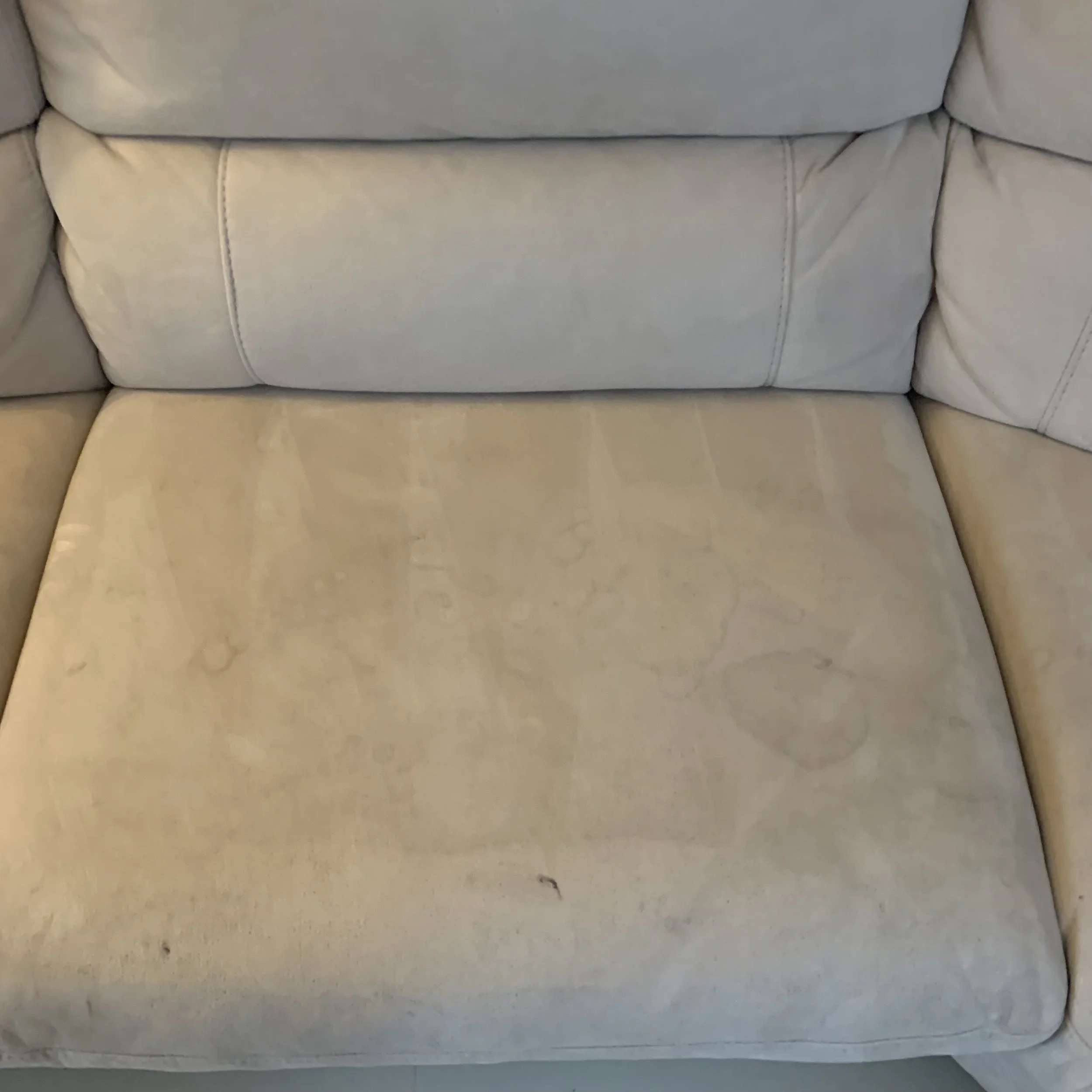 Close-up of a beige upholstered sofa with visible stains and discoloration on the seat cushion and backrest.