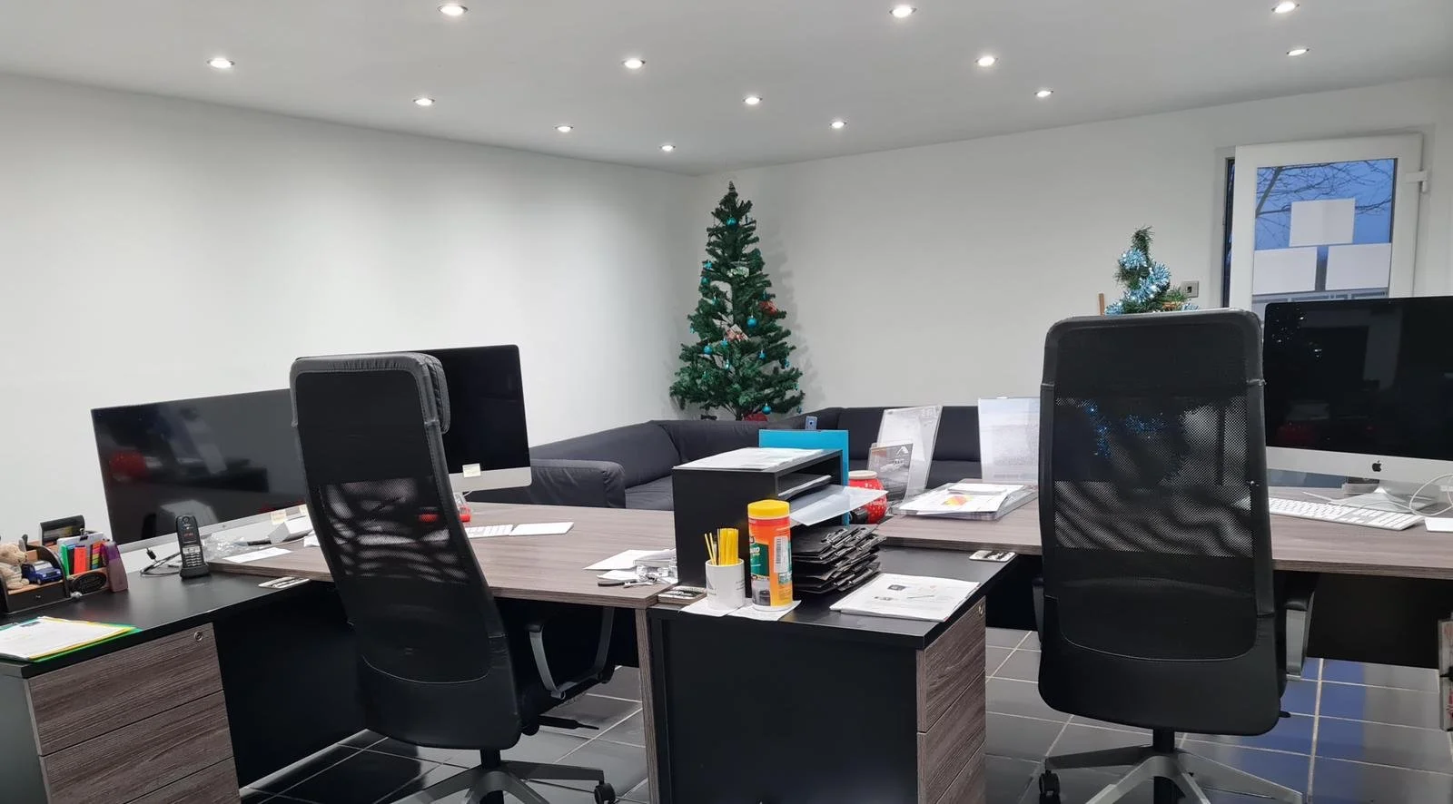 Office with two desks, computer monitors, office chairs, and Christmas trees in the background.