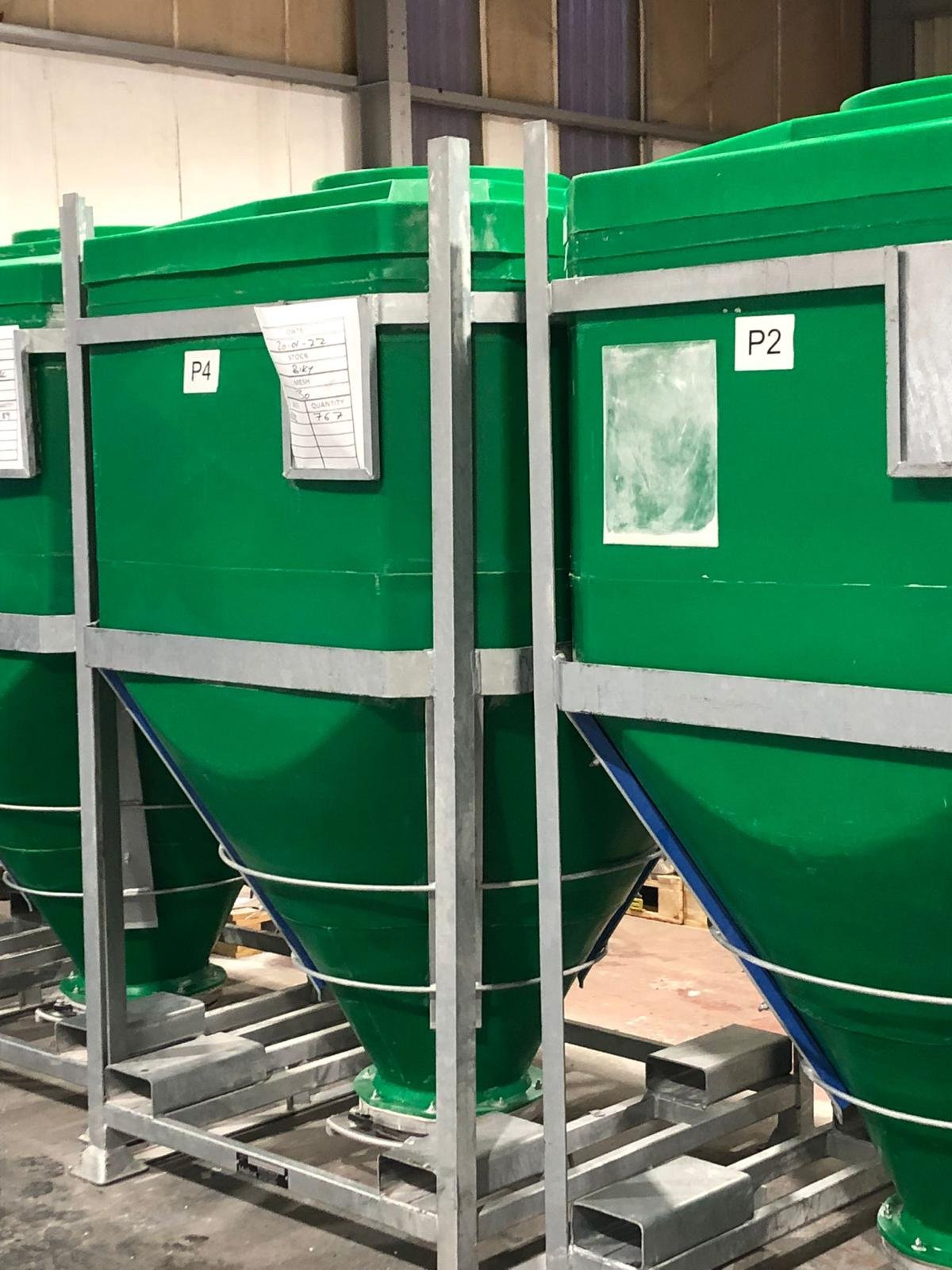 Stacked green industrial hoppers supported by a metal framework in a warehouse.