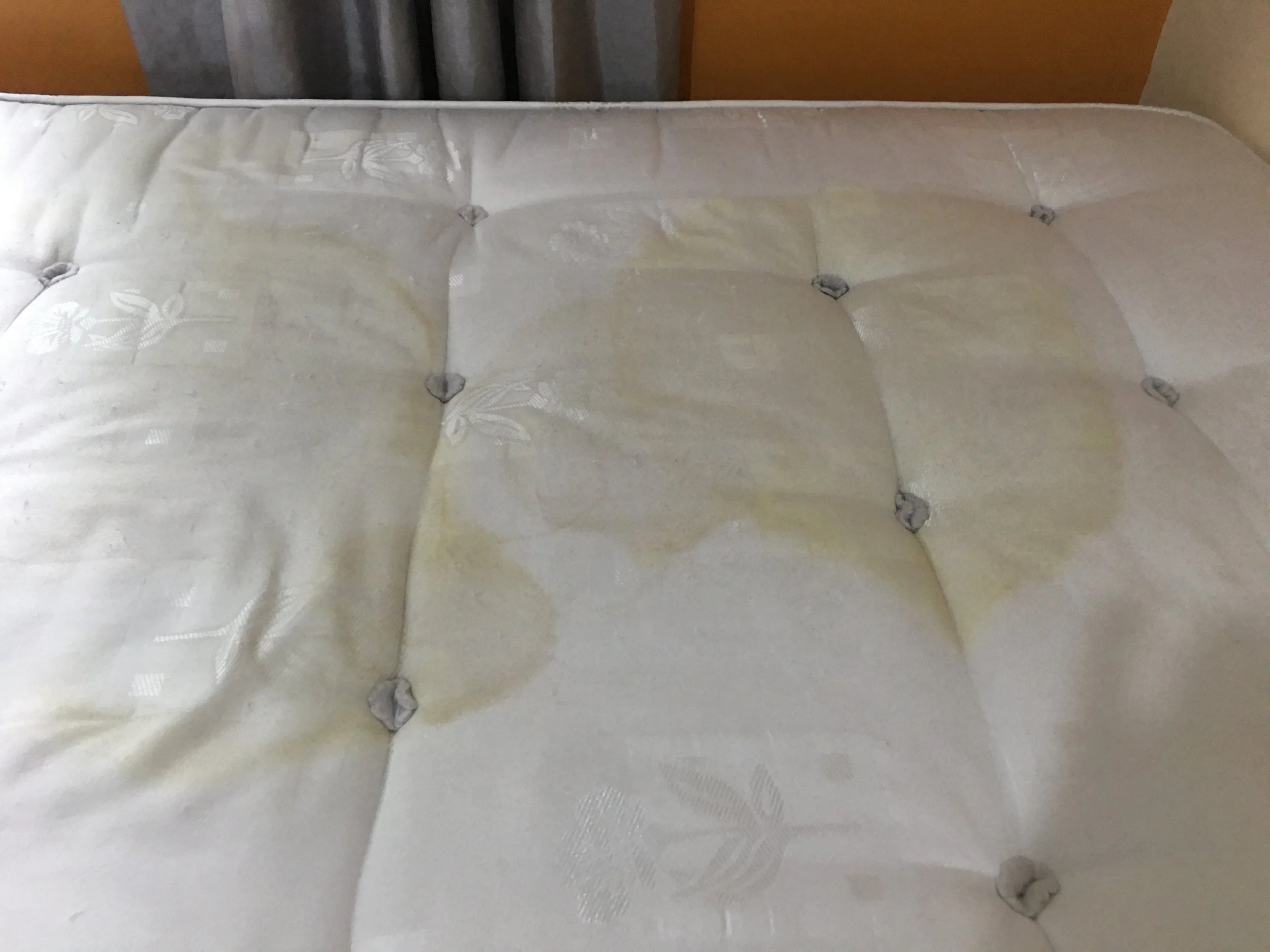A mattress with multiple yellowish stains on its white fabric surface.