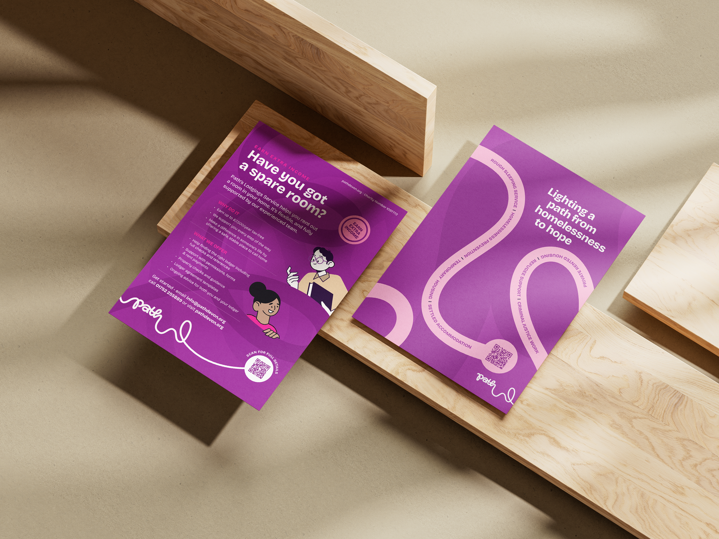 Brochures on a wooden table promoting pathways from homelessness to hope, with purple backgrounds, illustrations of people, and QR codes for more information.
