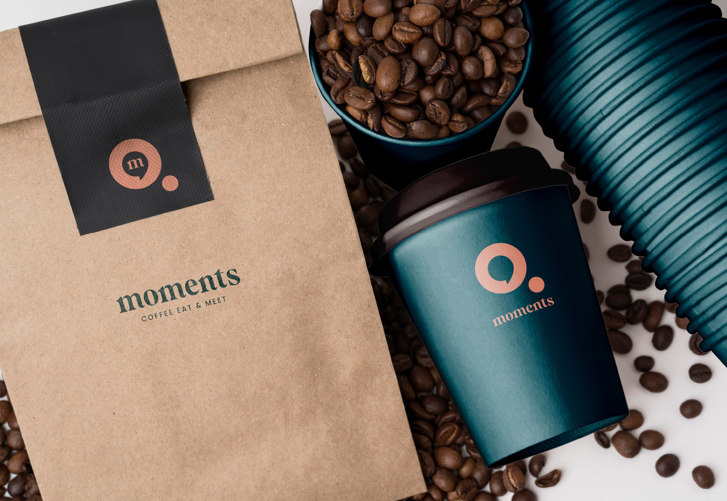 A package of Moments coffee, a blue coffee cup filled with coffee beans, a blue coffee sleeve, and scattered coffee beans on a white surface.