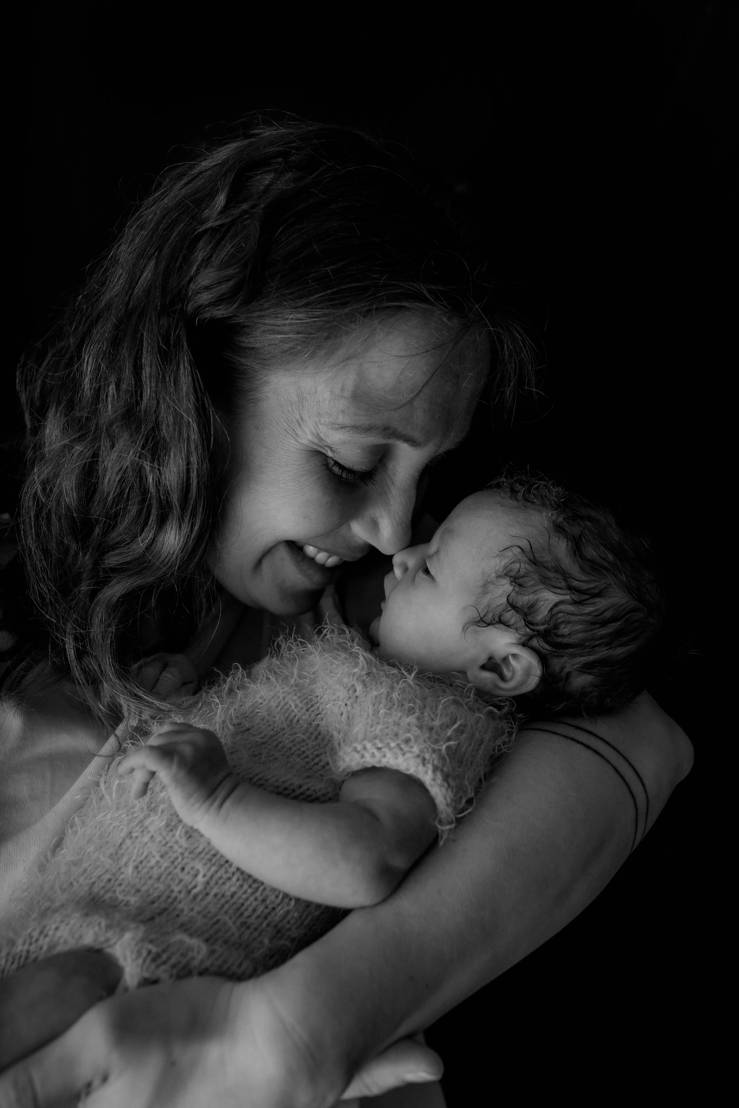 Schwarz-weiß-Foto einer Mutter, die ihr neugeborenes Baby liebevoll hält und an ihr schnuppert.