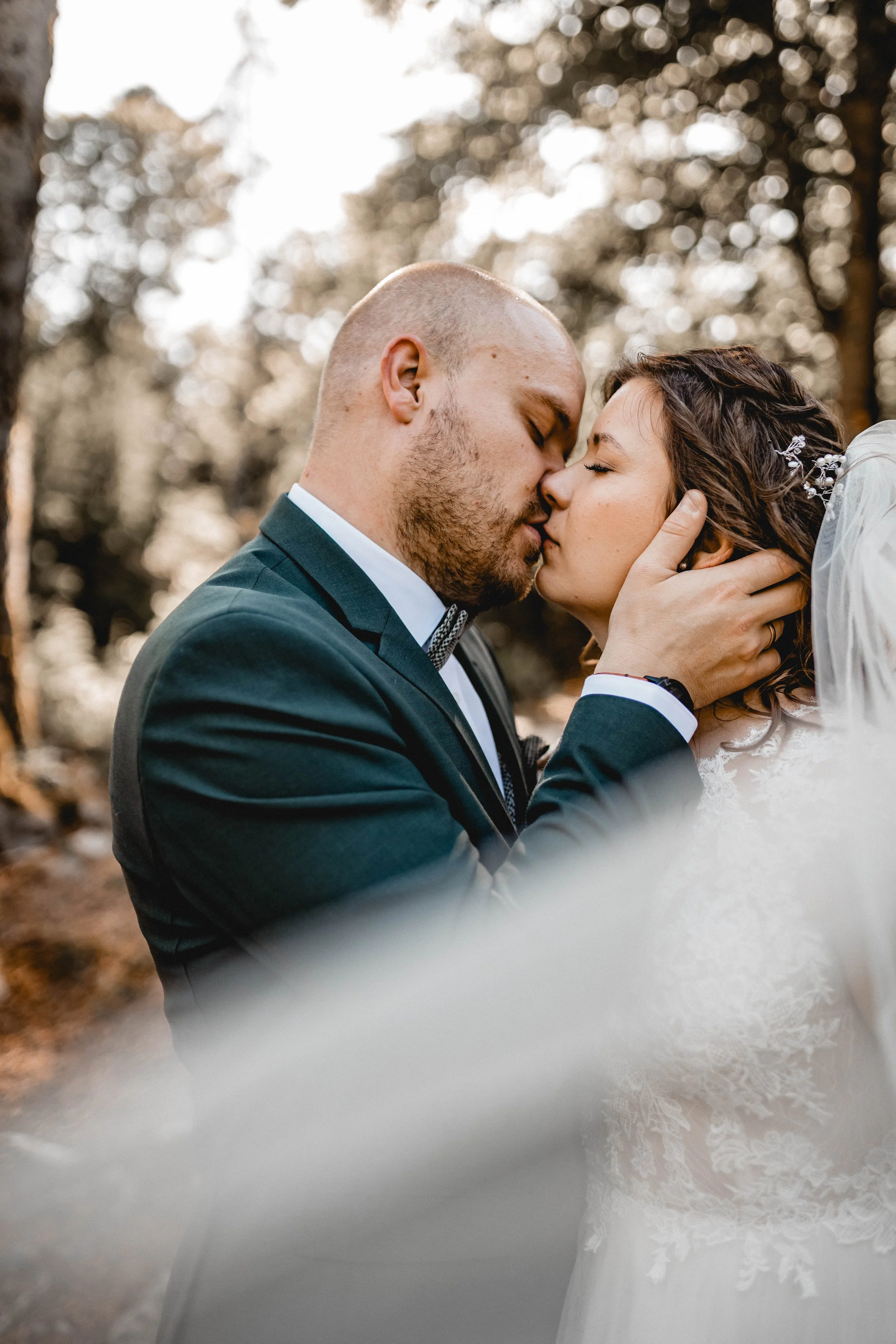 Ein Brautpaar bei einer Hochzeit im Freien, das sich küsst, mit Bäumen im Hintergrund und warmem Licht.
