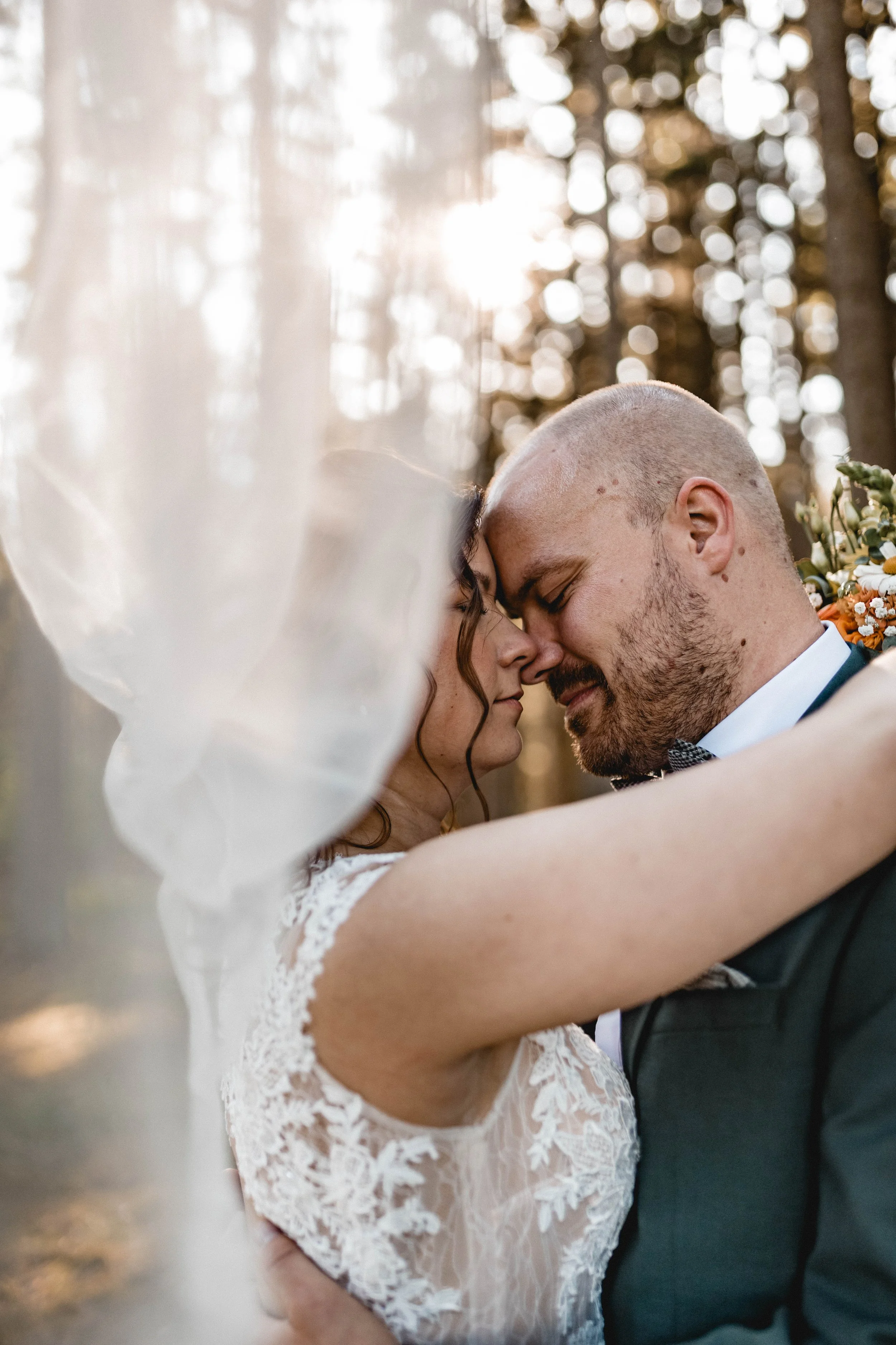 Ein Paar umarmt sich innig bei Sonnenuntergang im Wald, vermutlich während einer Hochzeit.