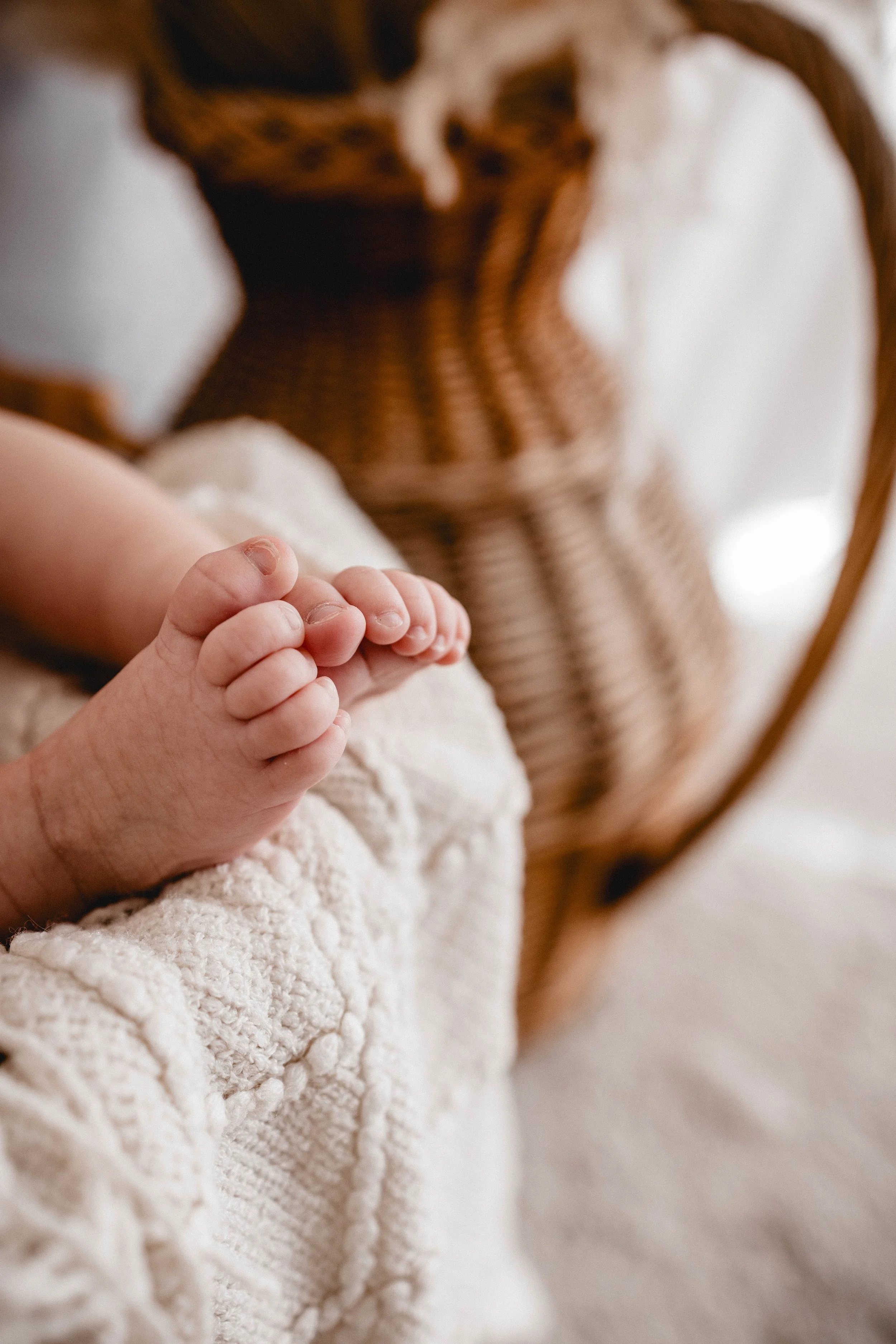 Nahaufnahme der zehen eines Babys, das auf einem weichen, cremefarbenen Tuch liegt, mit einem karamellfarbenen Korb im Hintergrund.