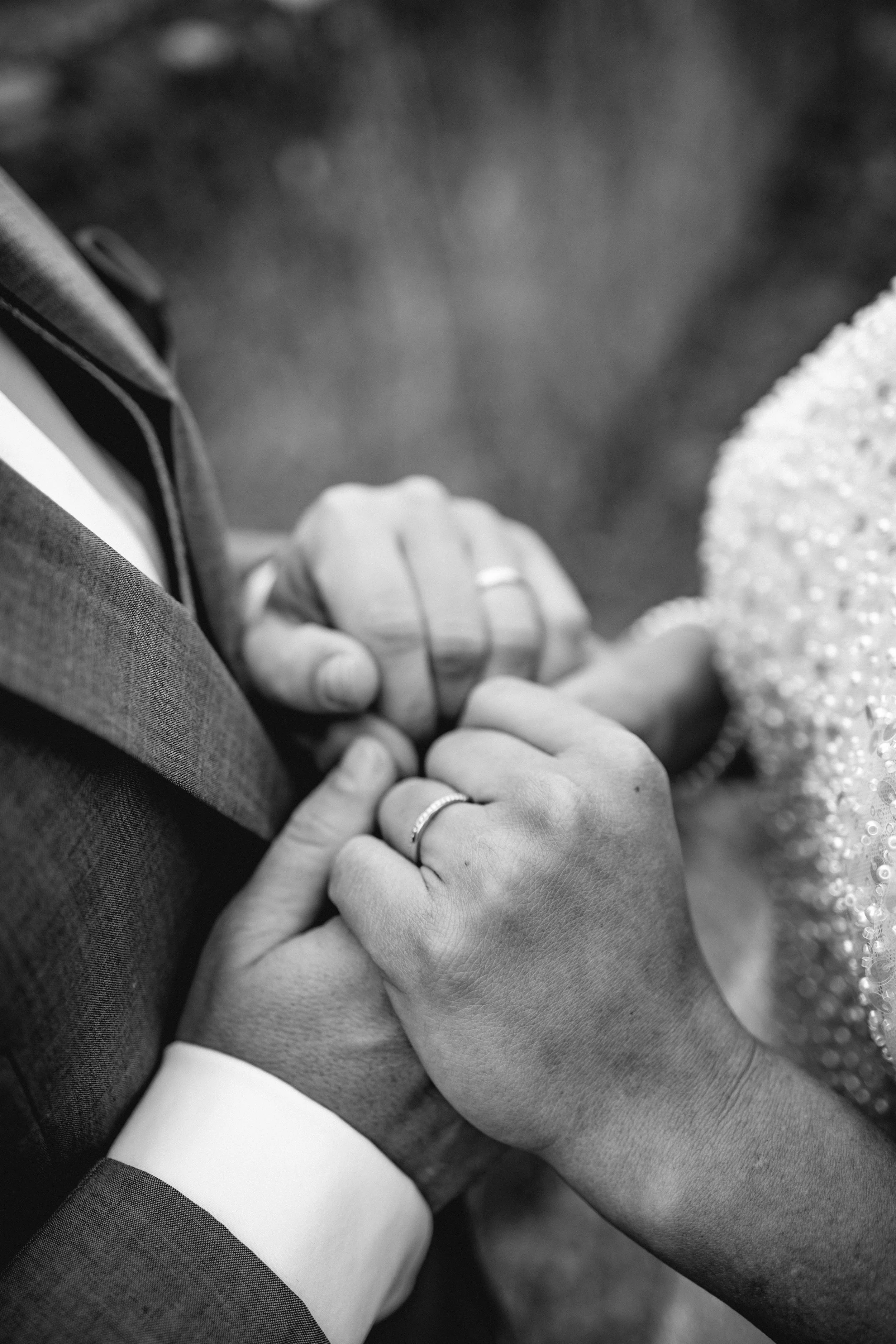 Nahaufnahme eines Paares, das sich an den Händen hält, bei einer Hochzeit. Beide tragen Ringe, und die Frau trägt ein funkelndes Kleid.
