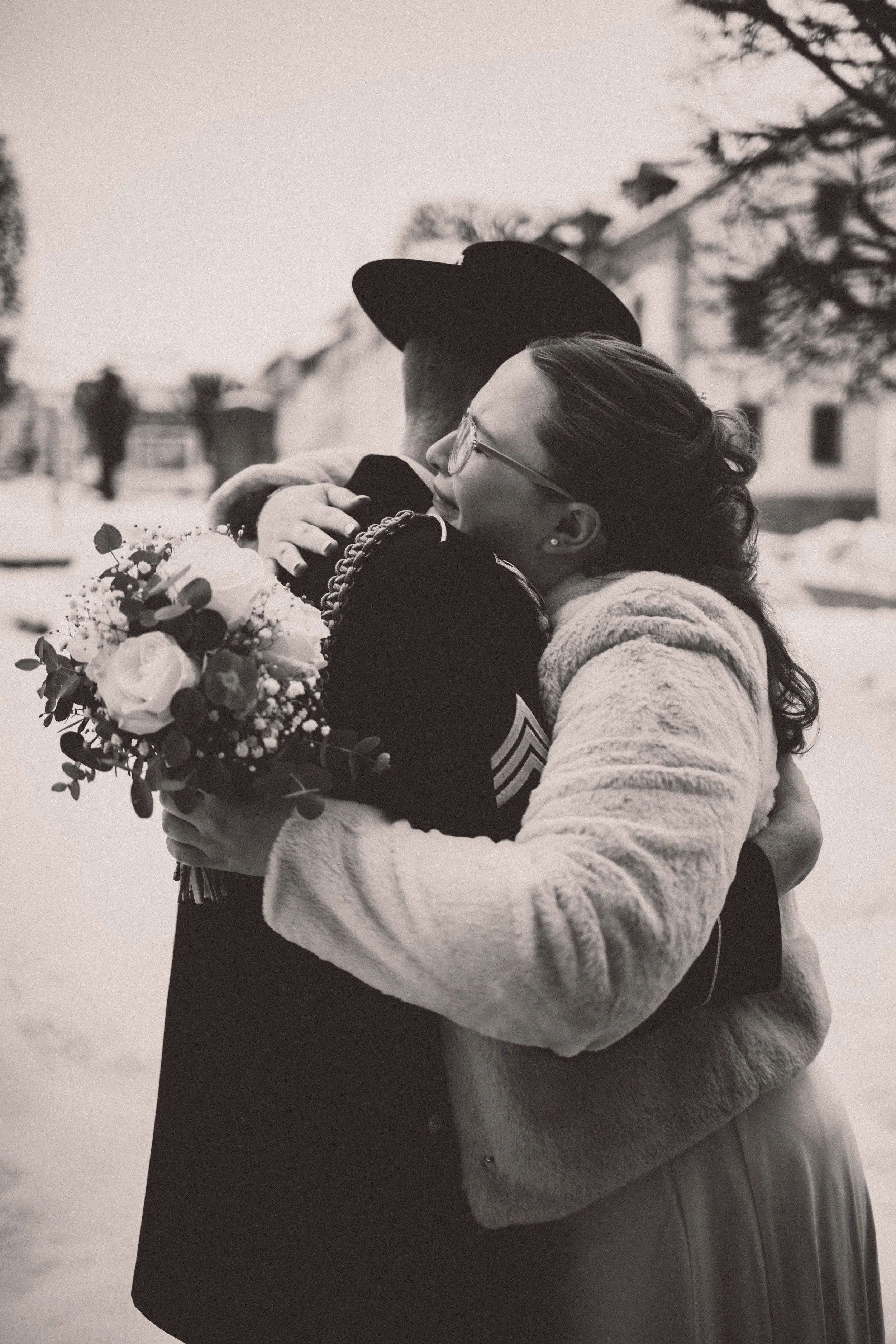 Zwei Menschen, eine Frau und ein Soldat, umarmen sich draußen im Schnee, die Frau hält einen Blumenstrauß.