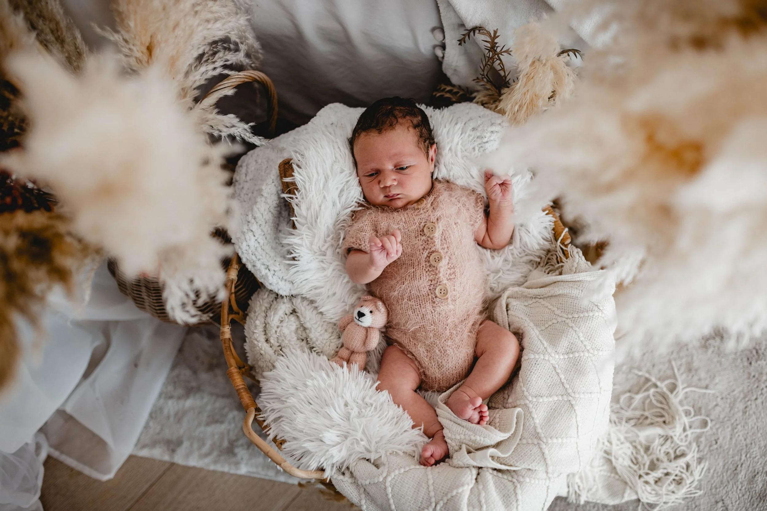 Kleiner neugeborener Baby in einem Korb, umgeben von weichen Decken und Pflanzen