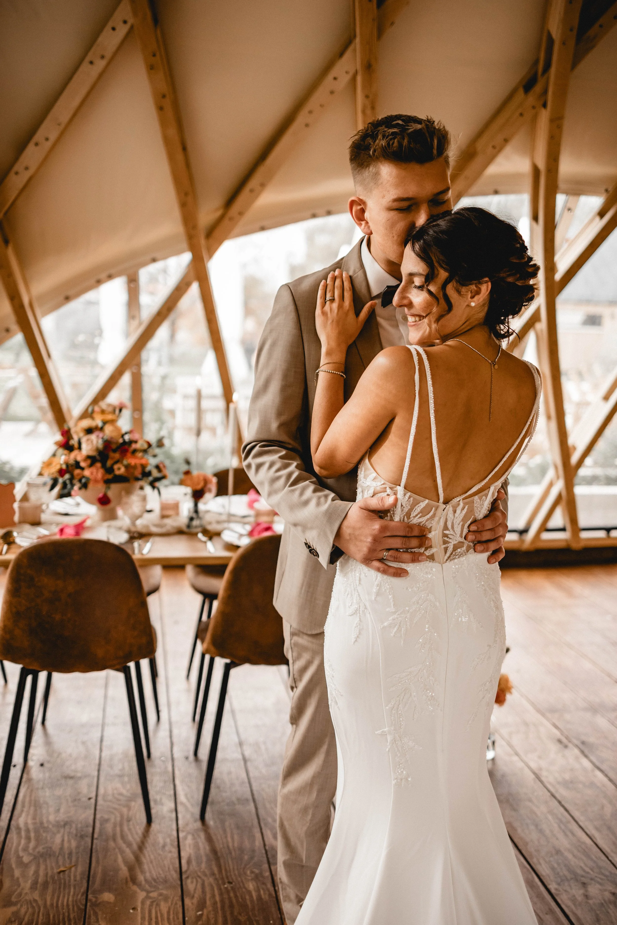 Ein glückliches Brautpaar tanzt bei einer bevorstehenden Hochzeit in einem rustikalen Holzgebäude mit Dekorationen und Blumen im Hintergrund.