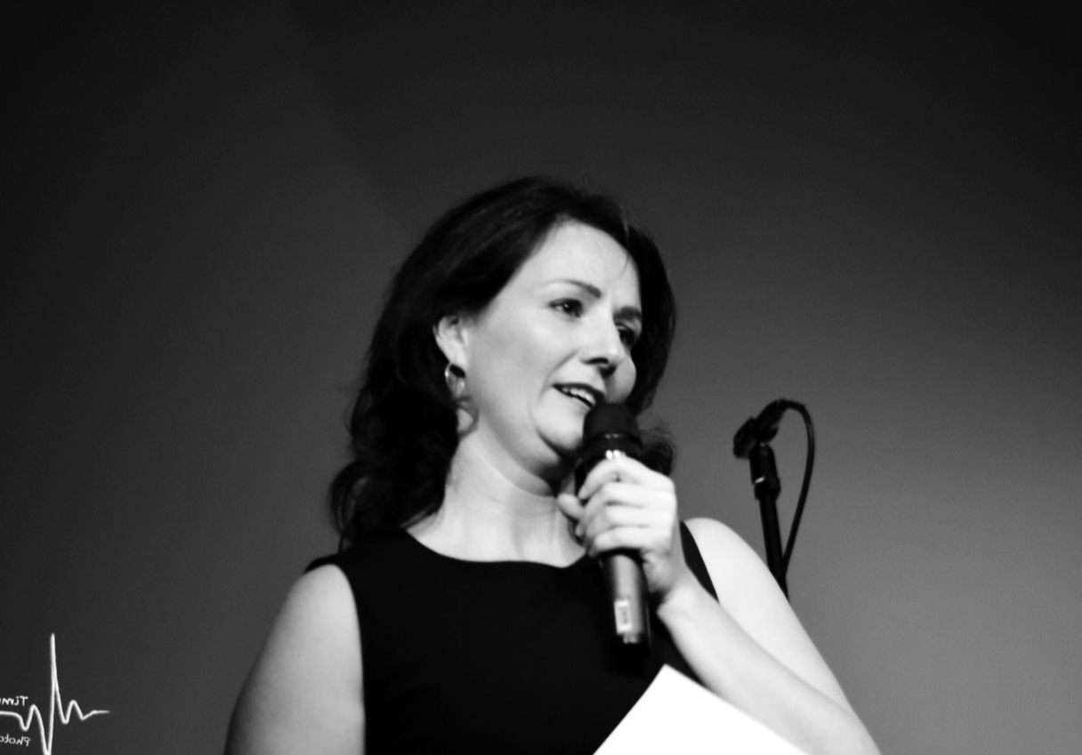 Schwarz-weiß Foto einer Frau beim Reden mit Mikrofon auf einer Bühne