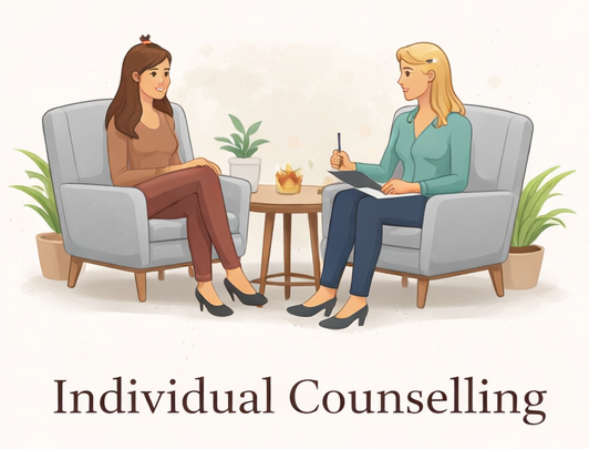 A woman in a brown dress and a woman in a blue shirt sitting on gray armchairs facing each other with a small table in between. The table has a potted plant, a lamp, and a decorative object. The setting is labeled "Individual Counselling."