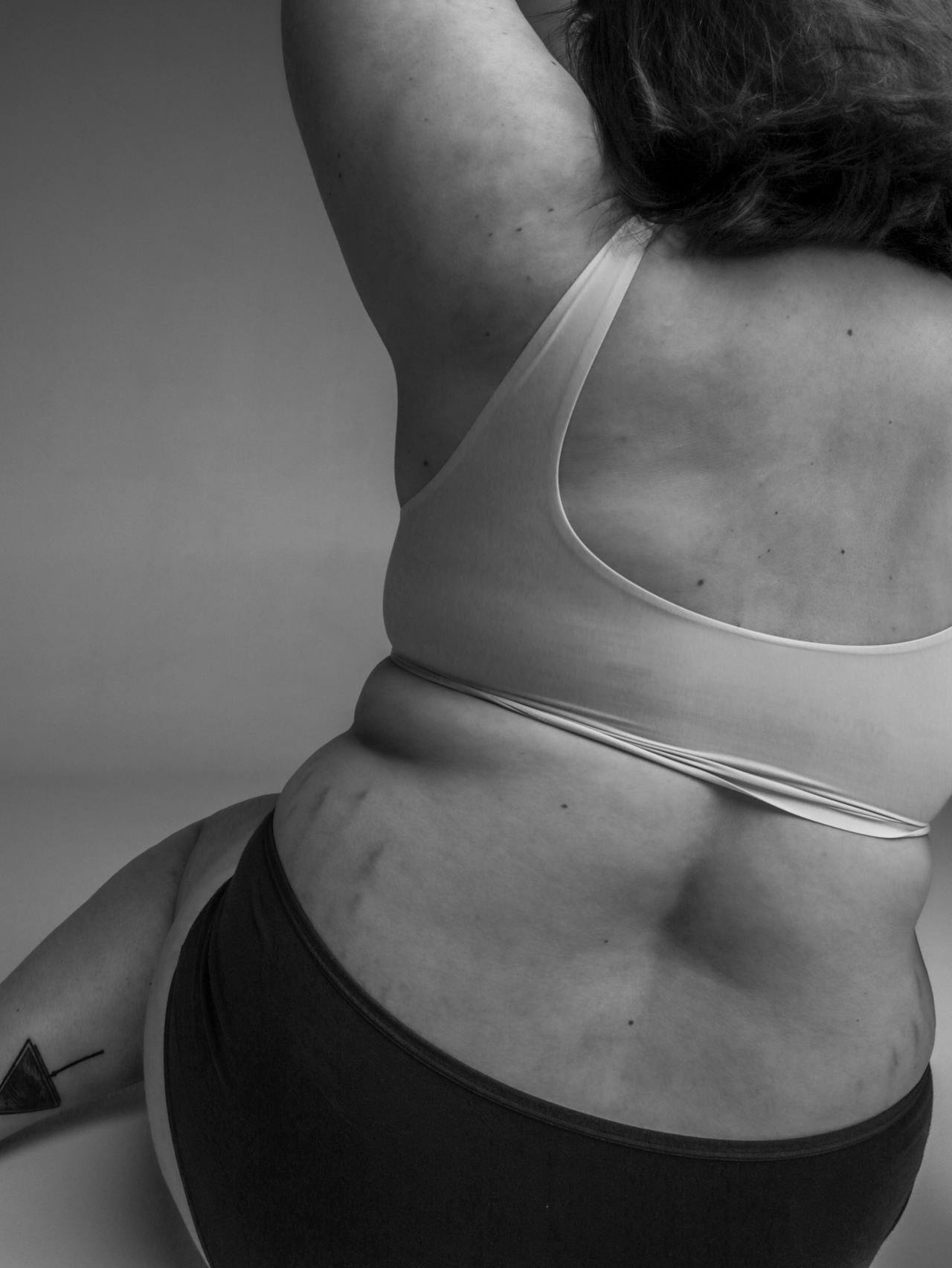 Close-up black and white photo of a woman's midsection, showing her belly and side, wearing a sports bra and shorts.