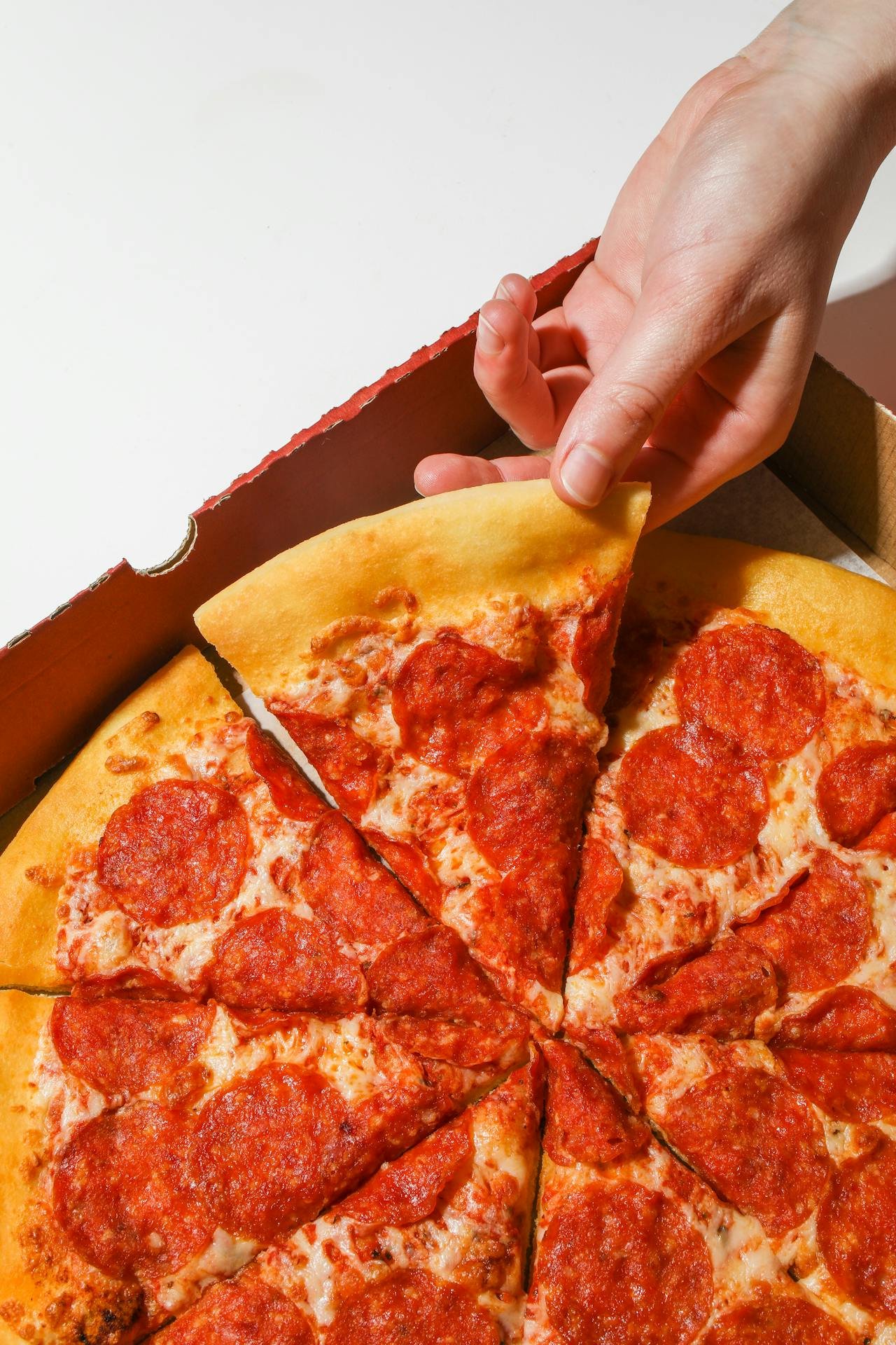 Close-up of a hand grabbing a slice of pepperoni pizza, with other slices on a pizza box.