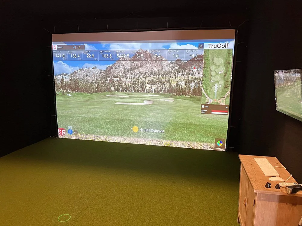 Indoor golf simulator displaying a golf course with mountains and trees in the background, with various game statistics and a map of the hole.