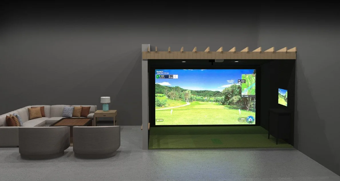 Indoor golf simulator setup with a large screen displaying a golf course, two smaller screens, and a golf mat, next to a modern sofa and side table with a lamp in a lounge area.