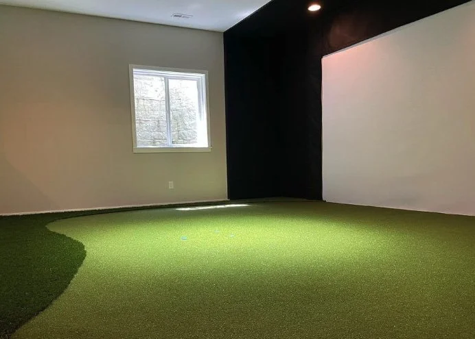 Empty room with a small window, beige wall, dark accent wall, and artificial green turf floor.