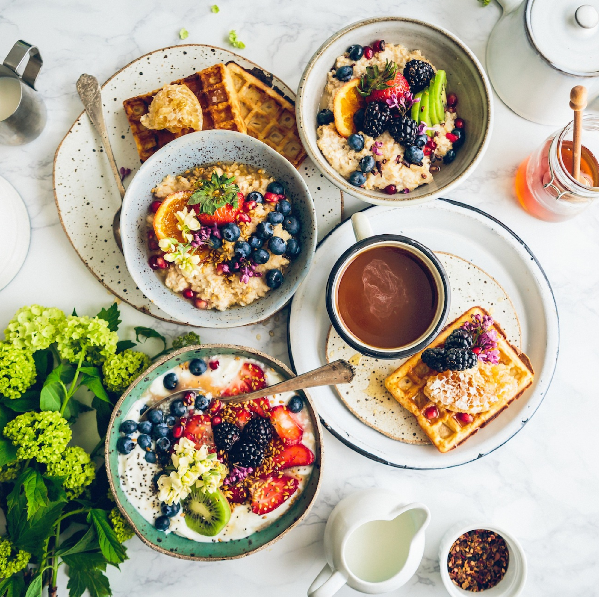 Büfett mit Waffeln, Haferbrei mit Beeren und Obst, sowie verschiedenen Toppings und Getränken auf einem weißen Marmortisch, isländische...