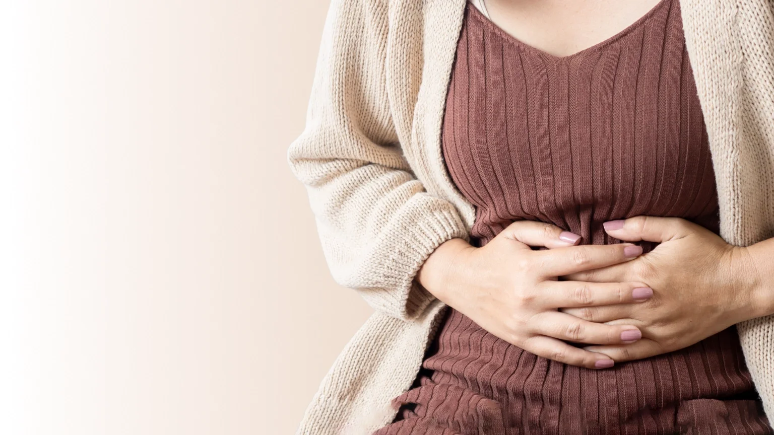 Eine Frau hält sich den Bauch, um Schmerzen oder Unwohlsein im Magenbereich anzuzeigen.